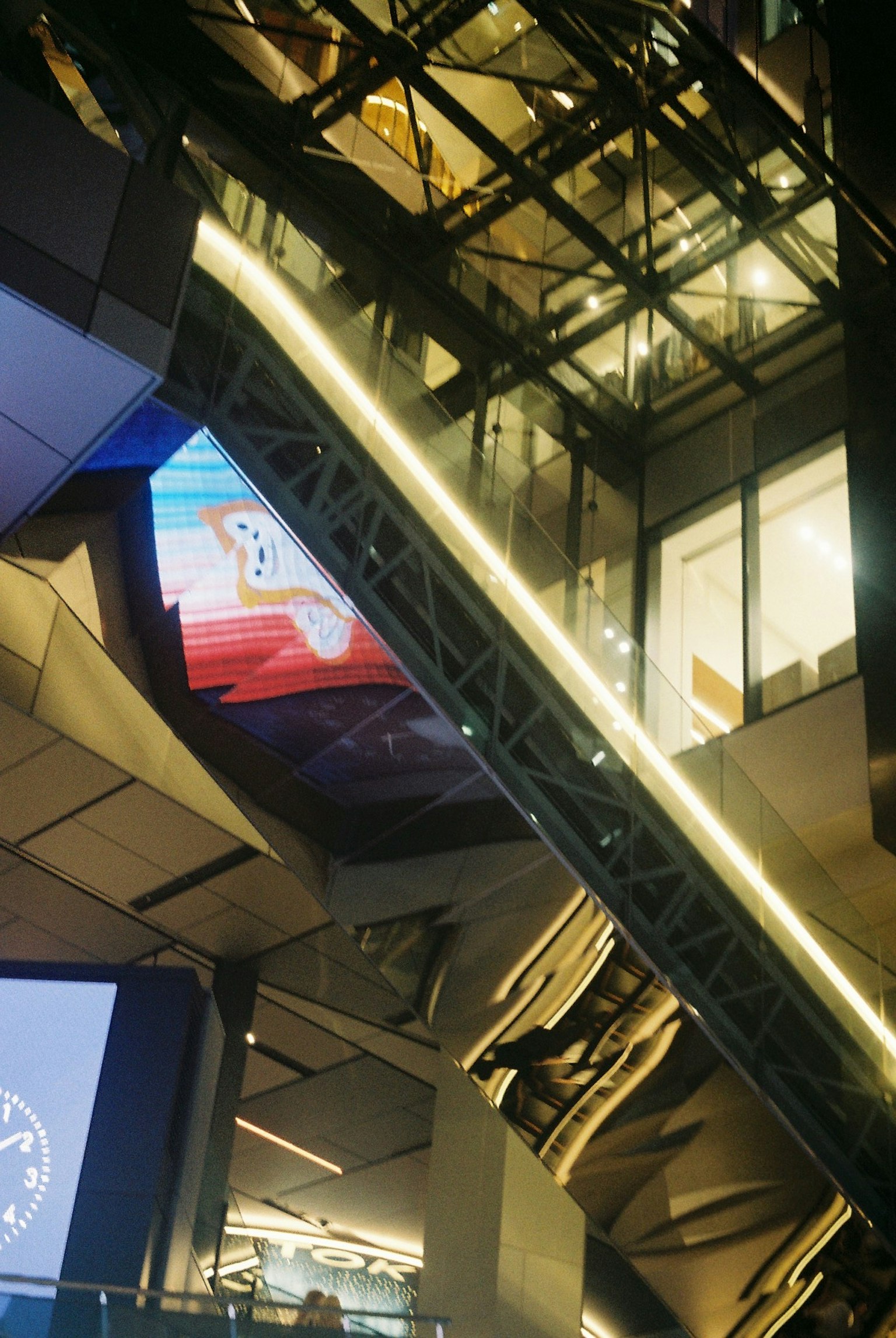 Tampilan interior gedung modern dengan eskalator dan pencahayaan yang mencolok dalam arsitektur kaca