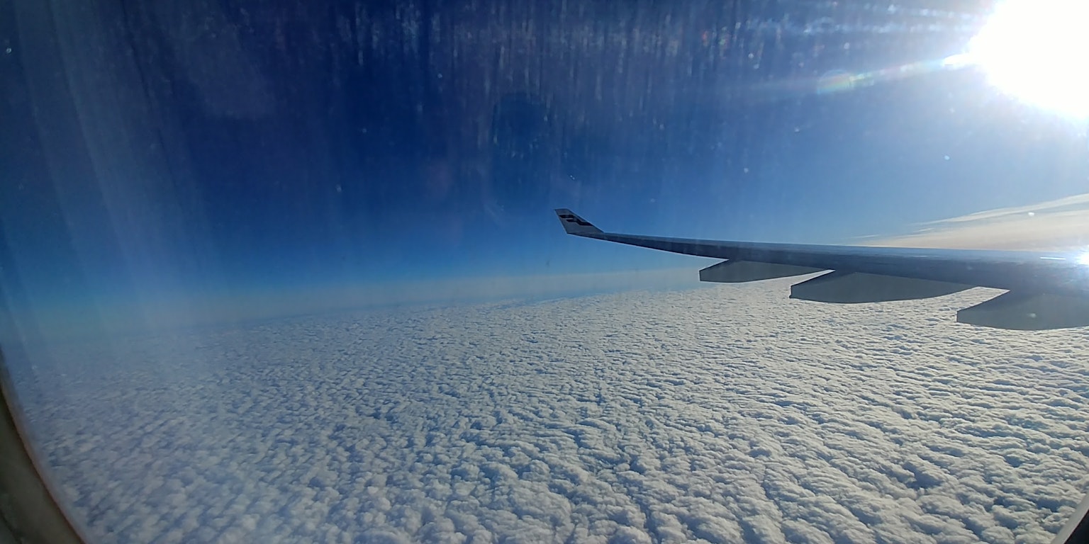 Pemandangan dari jendela pesawat dengan laut awan dan langit biru sayap pesawat
