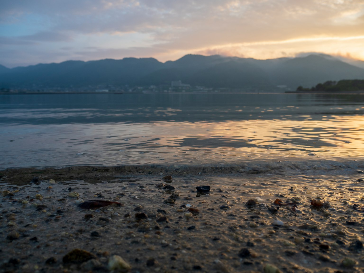 ทิวทัศน์ชายหาดที่เงียบสงบพร้อมท้องฟ้ายามพระอาทิตย์ตกและภูเขาที่สะท้อนในน้ำ
