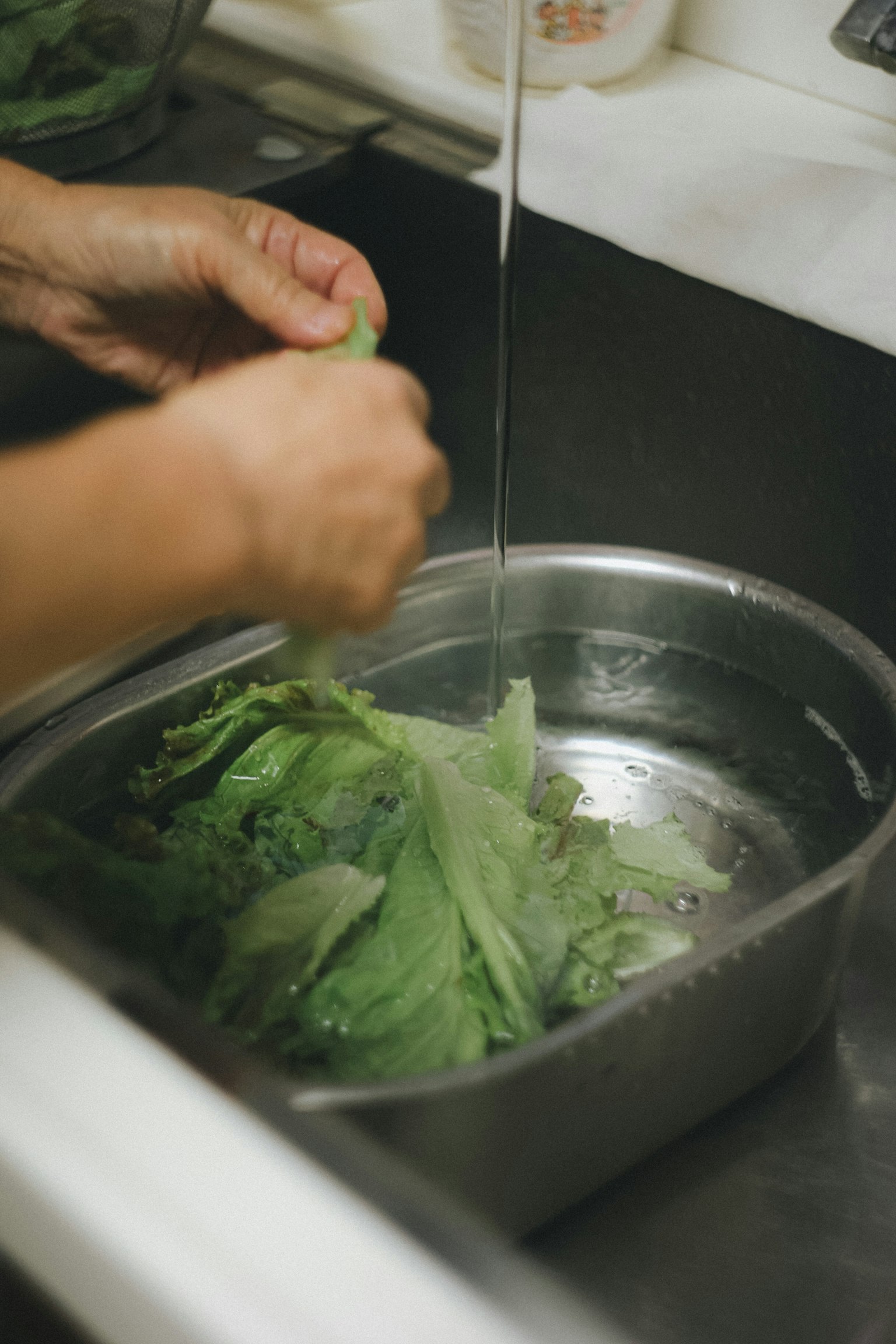 手で葉物野菜を洗っている様子 水が流れているシンクの中