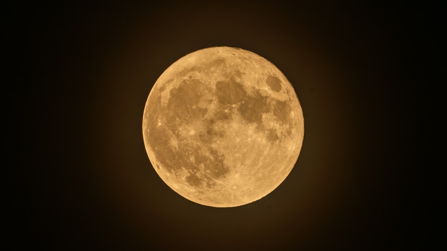 A bright orange full moon in a dark night sky