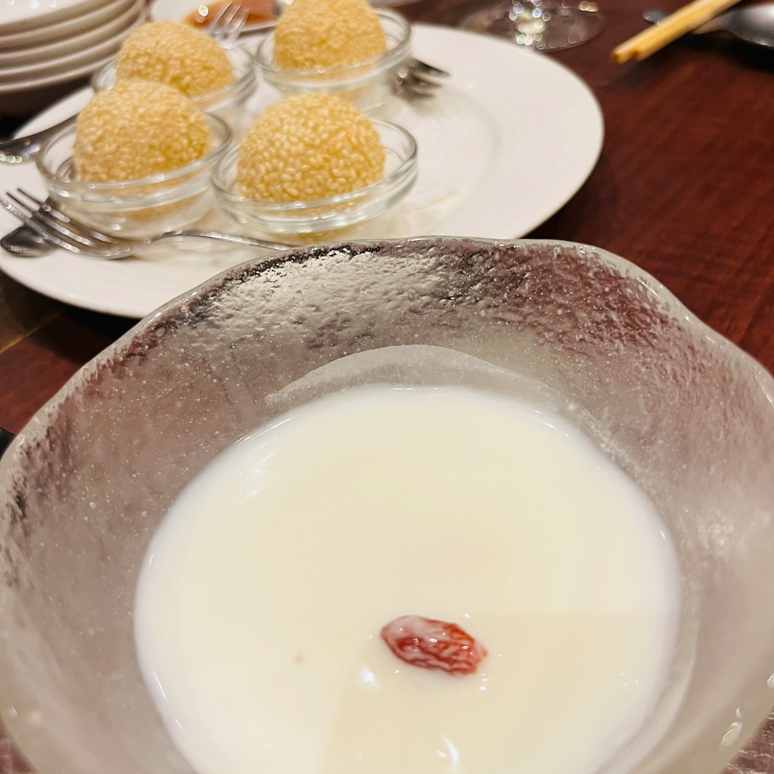 白色湯中漂浮著枸杞的甜點，背景中有四個芝麻球