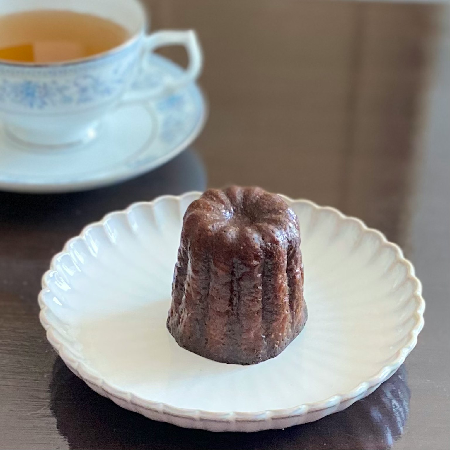 Canelé su un piatto bianco con una tazza di tè sullo sfondo