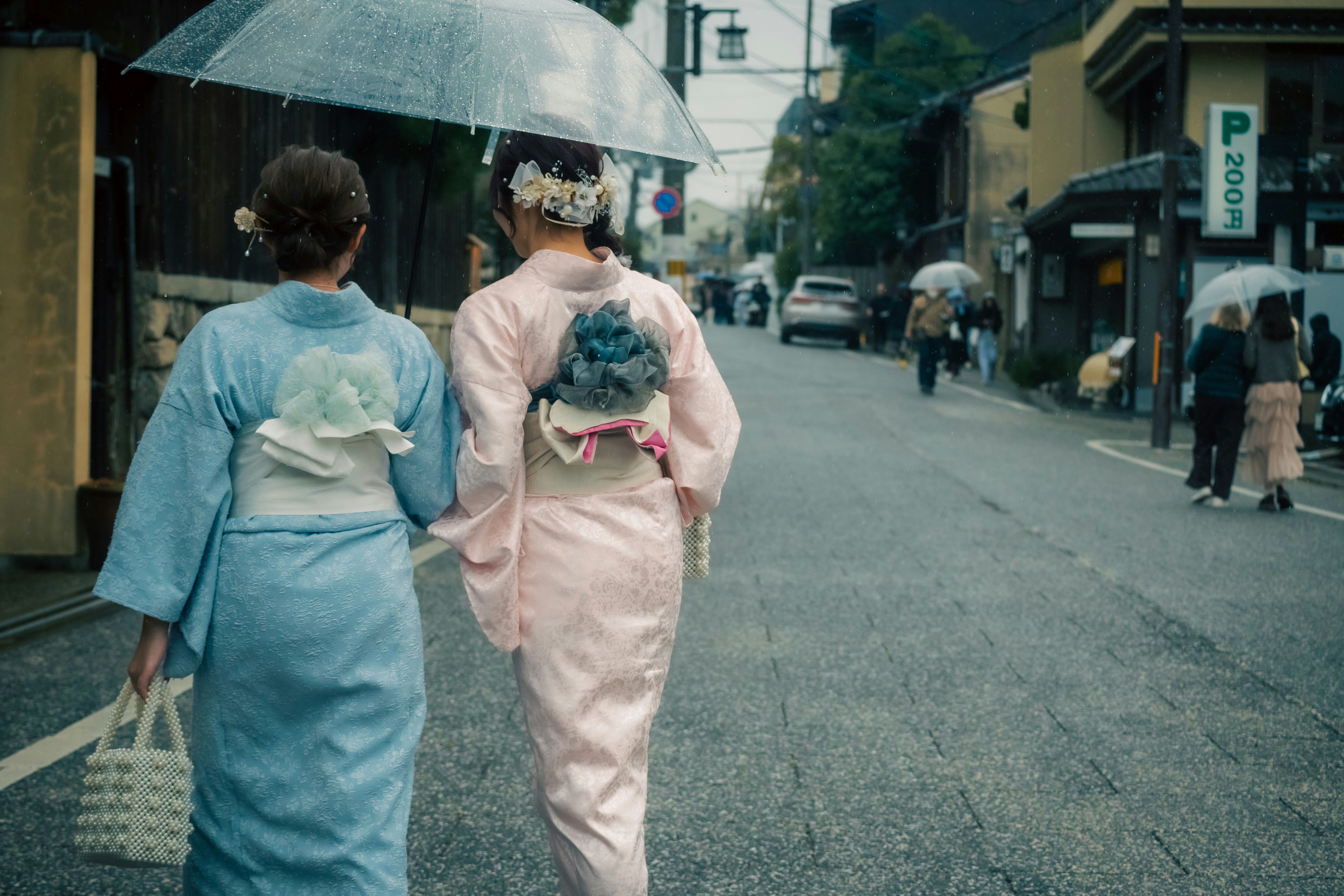 雨の路地を歩く着物姿の人たちの後ろ姿