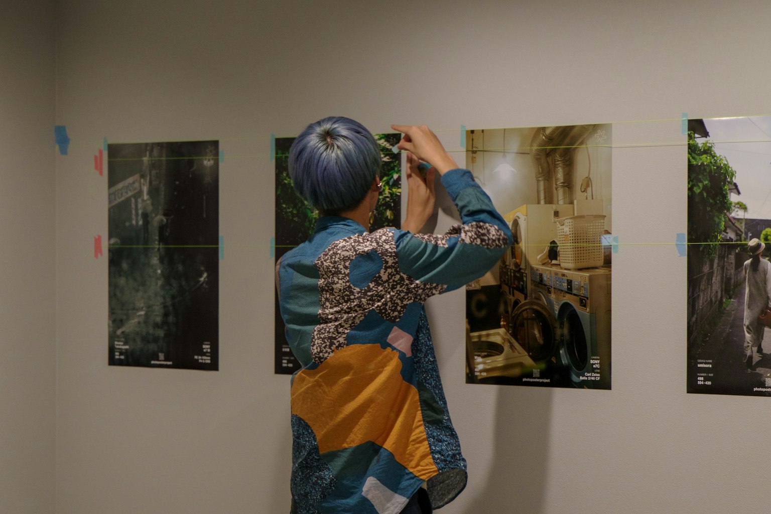 파란 머리를 가진 사람이 벽에 포스터를 걸고 있는 모습 화려한 셔츠를 입고 있음