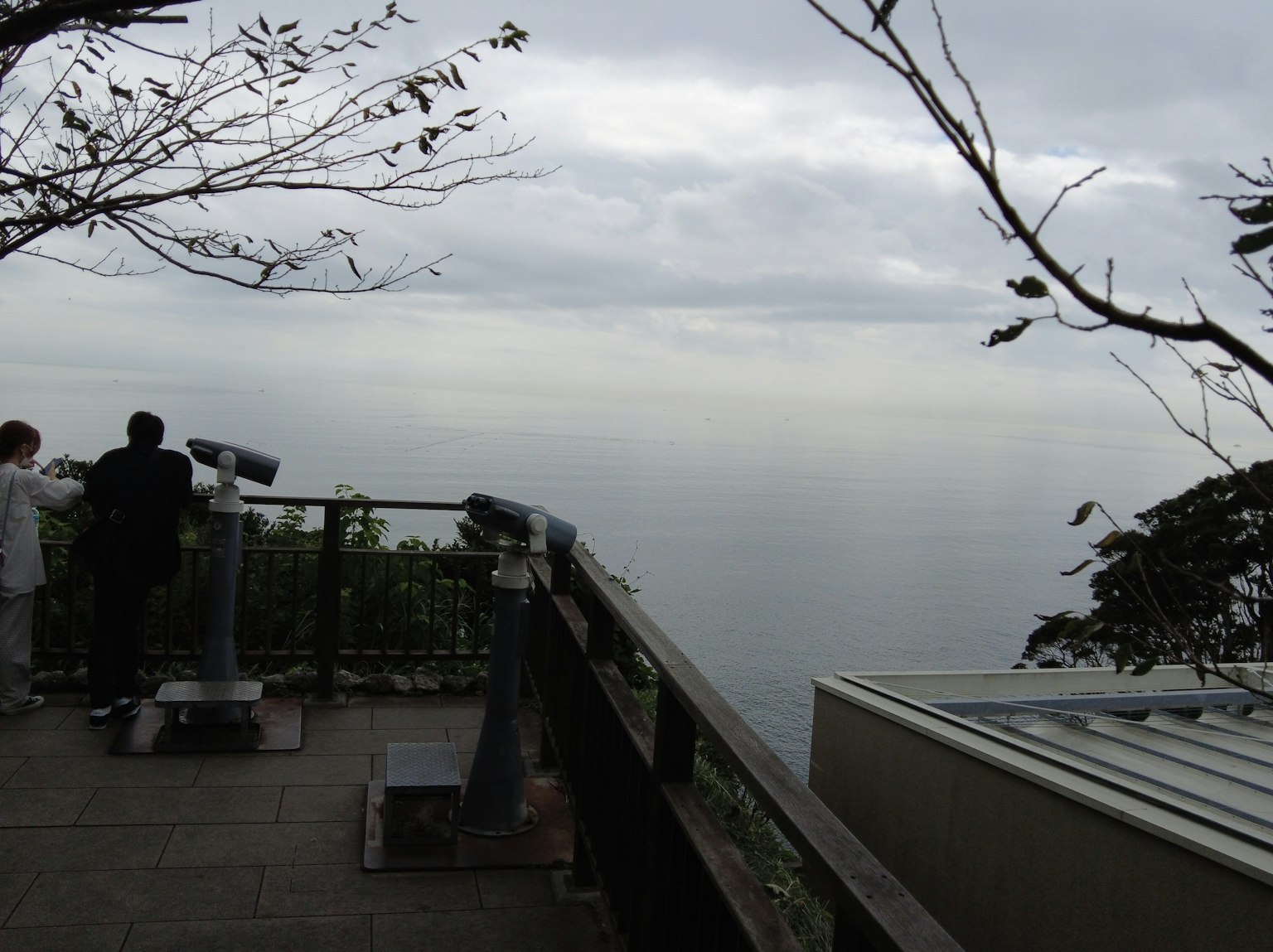 Menschen auf einer Aussichtsplattform mit Blick auf das Meer und bewölktem Himmel