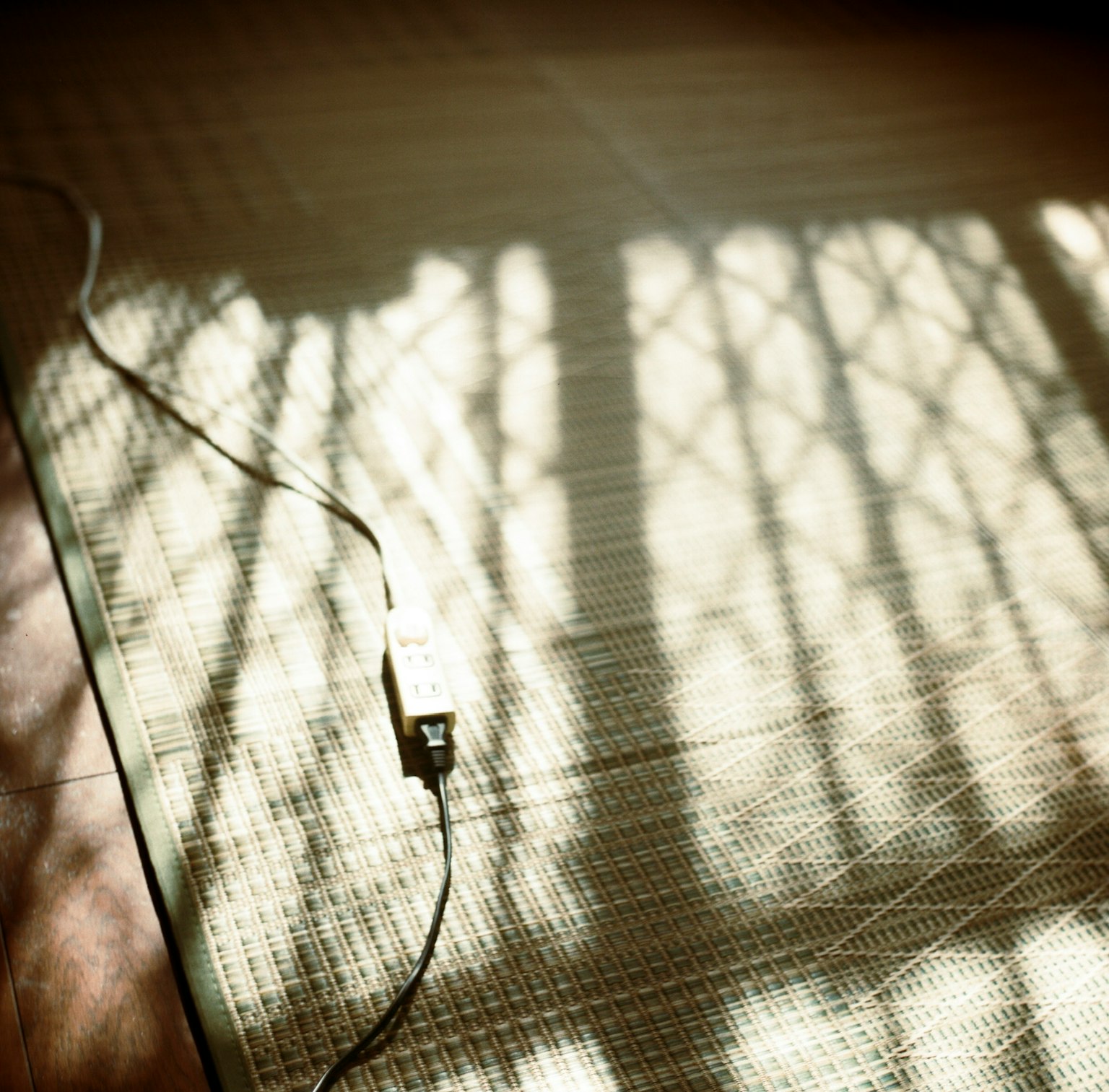 光が差し込む部屋の床に映る影と電源コード