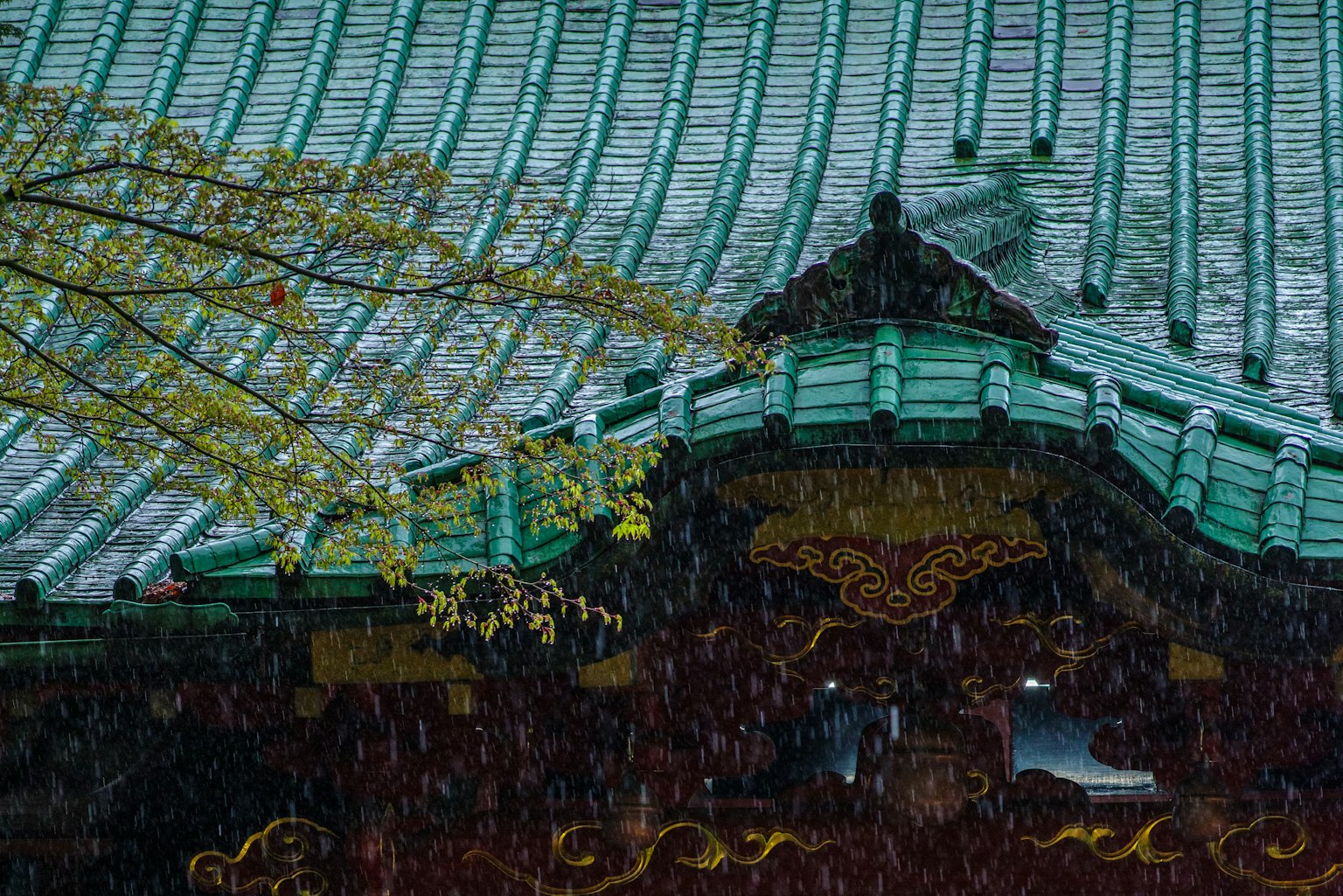 Toit d'un sanctuaire japonais traditionnel avec des tuiles vertes et des décorations dorées sous la pluie