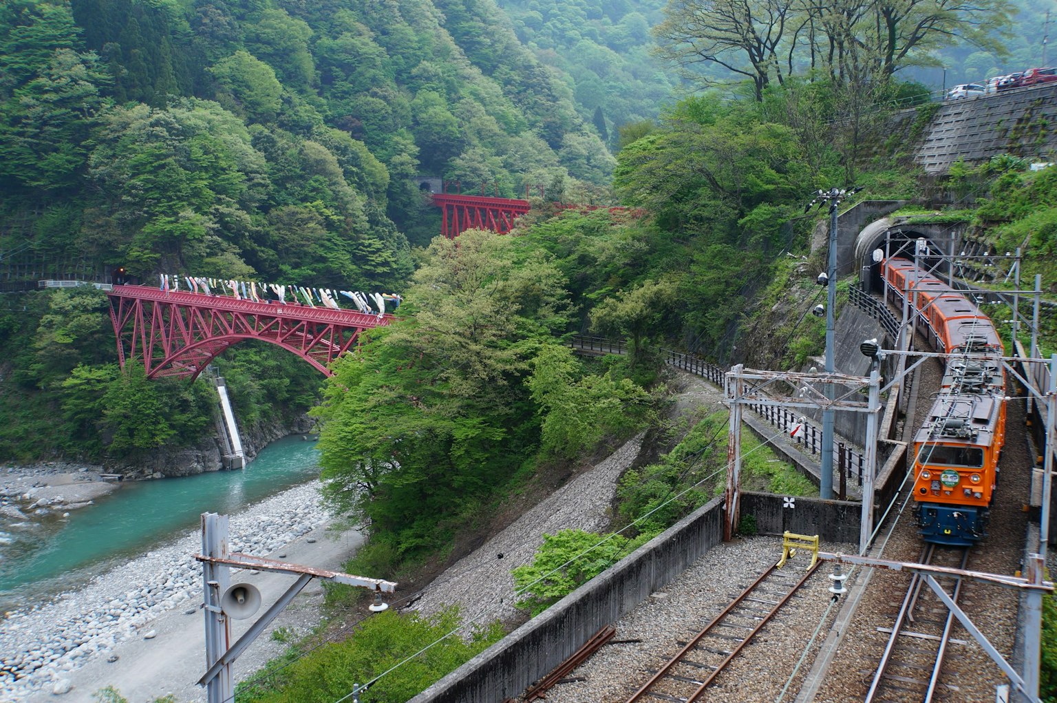 Vue panoramique d'un train et d'un pont rouge entourés de montagnes verdoyantes