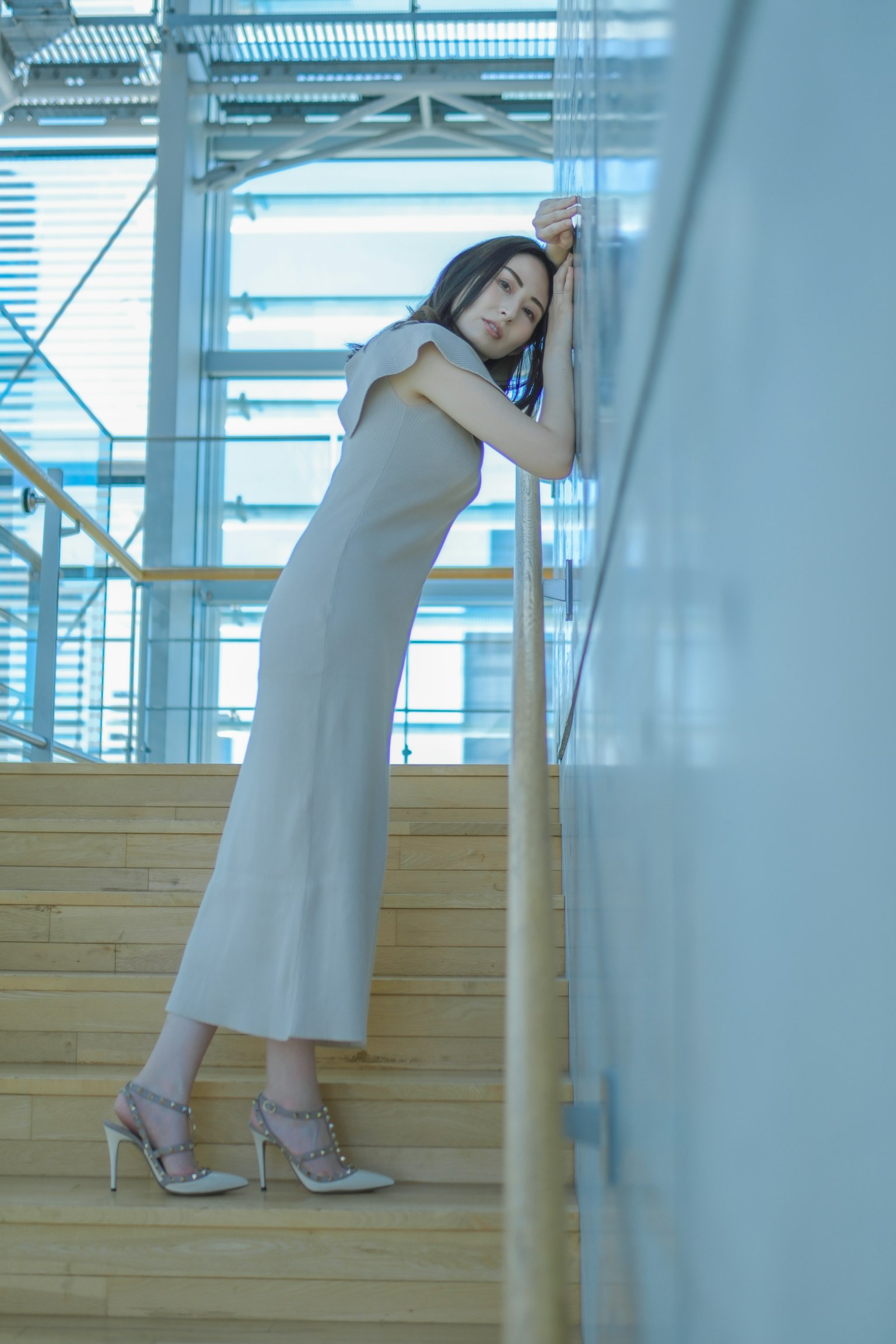Una donna appoggiata a un muro su una scala indossando un vestito semplice e tacchi alti