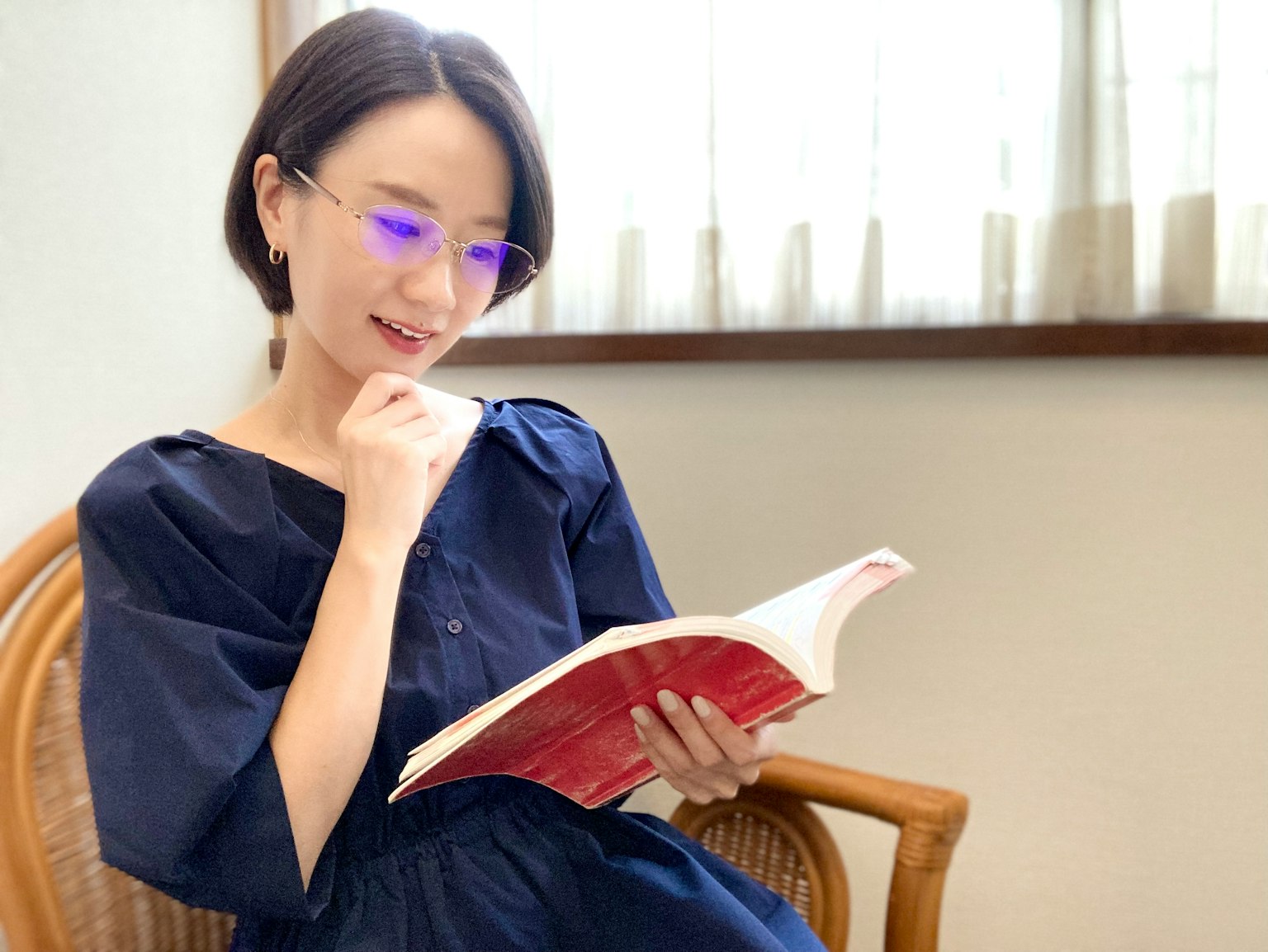 Mujer leyendo un libro junto a la ventana, con gafas azules, luz natural