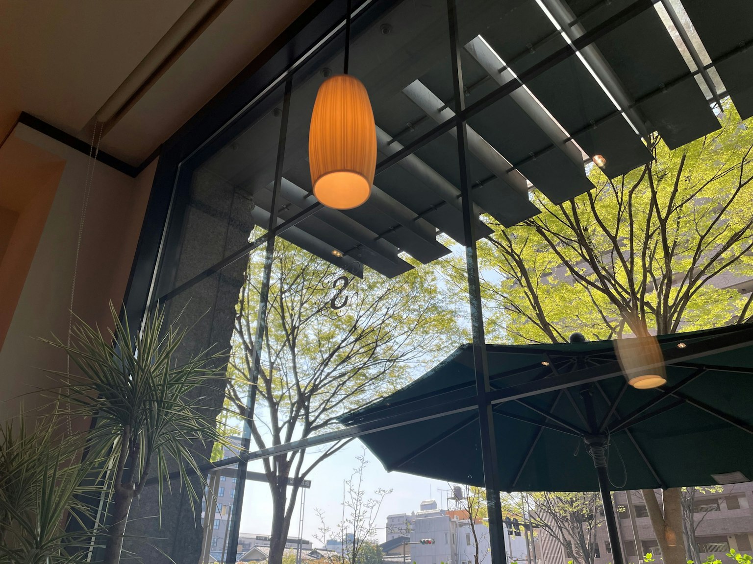 Interior kafe dengan lampu gantung dan pohon hijau terlihat melalui jendela besar