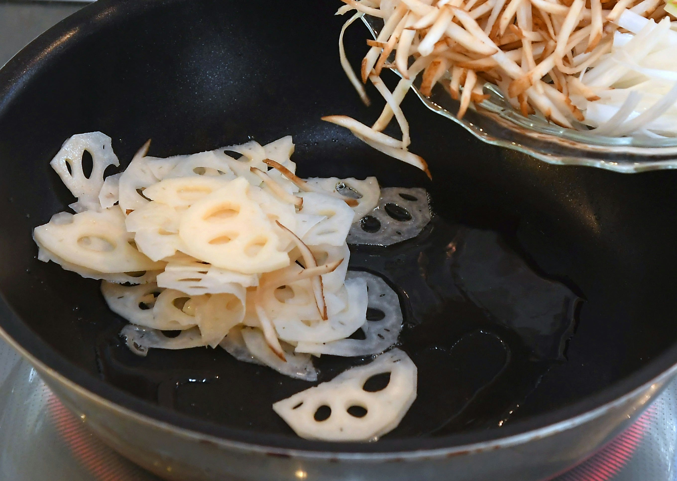 蓮根の薄切りを炒めるフライパンの上の料理