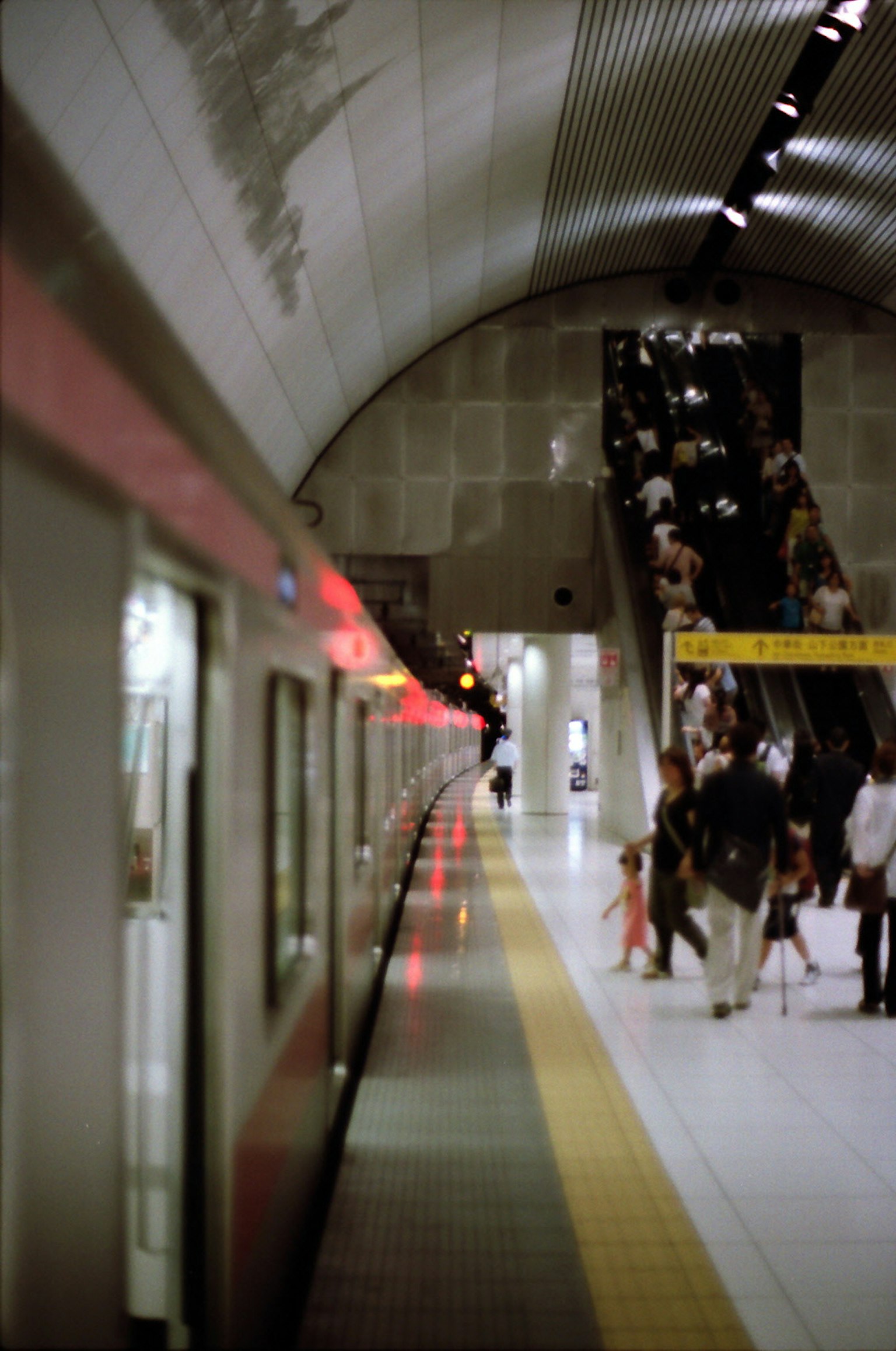 U-Bahn-Plattform mit einem stehenden Zug und Fahrgästen, die die Rolltreppe benutzen