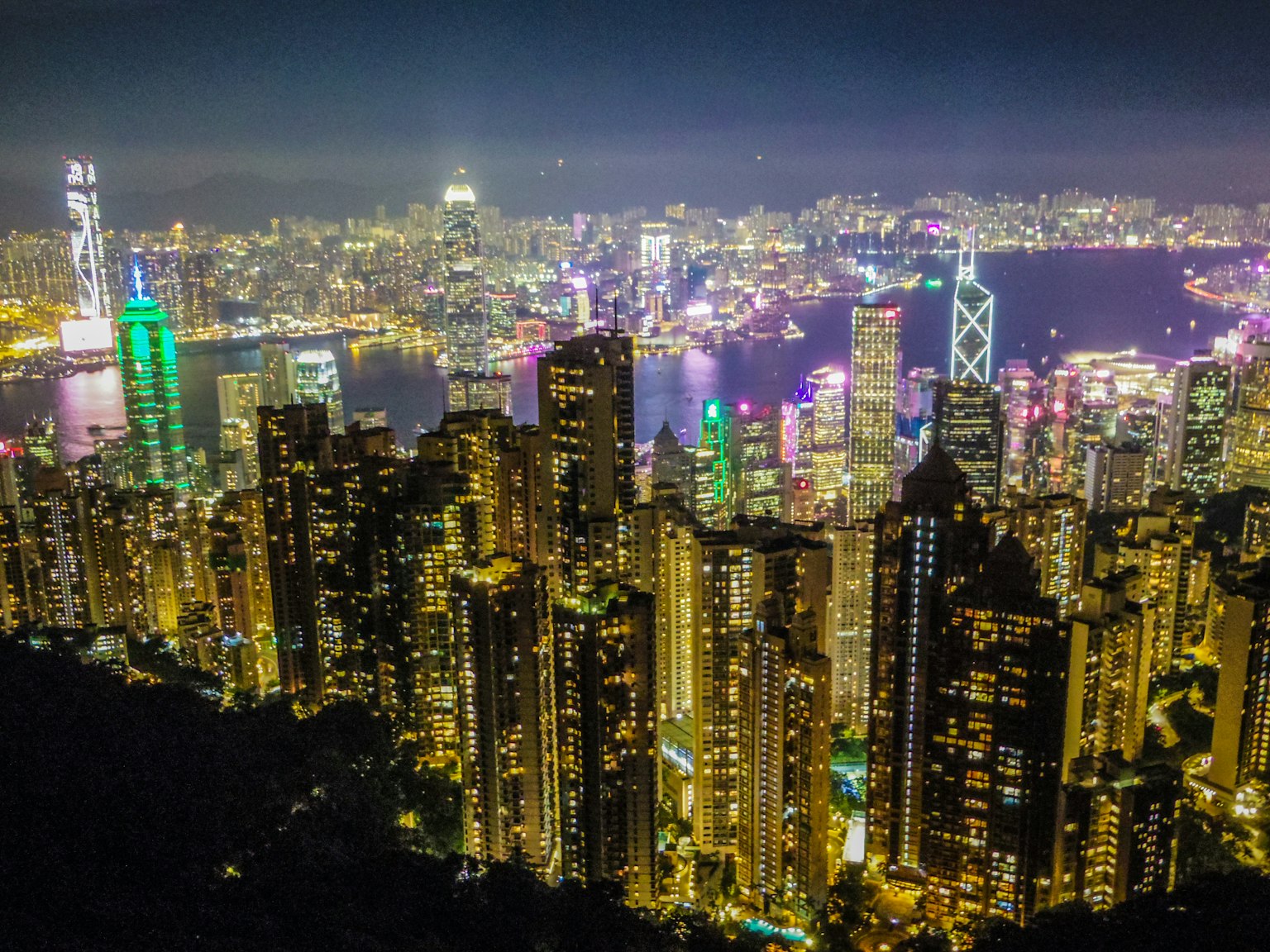 夜間的香港天際線全景，高樓大廈燈火輝煌，港口上色彩斑斓的倒影
