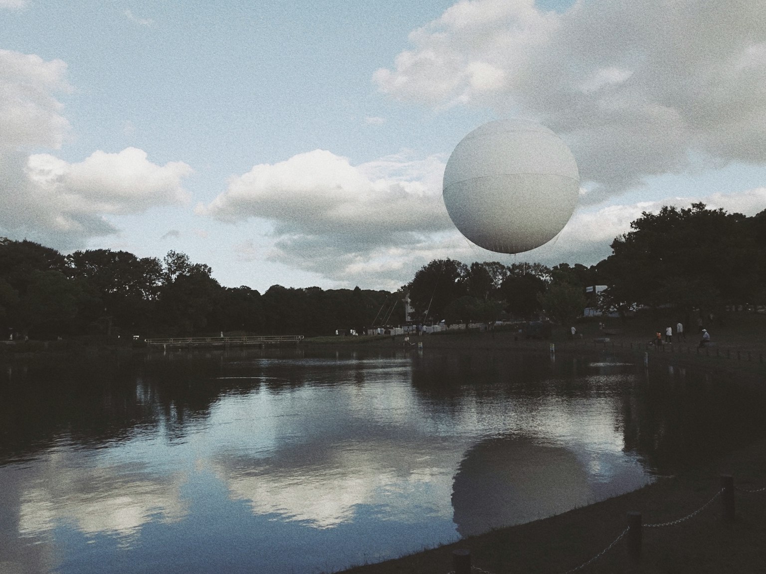 Eine große weiße Kugel schwebt über einem ruhigen See unter einem blauen Himmel mit Wolken
