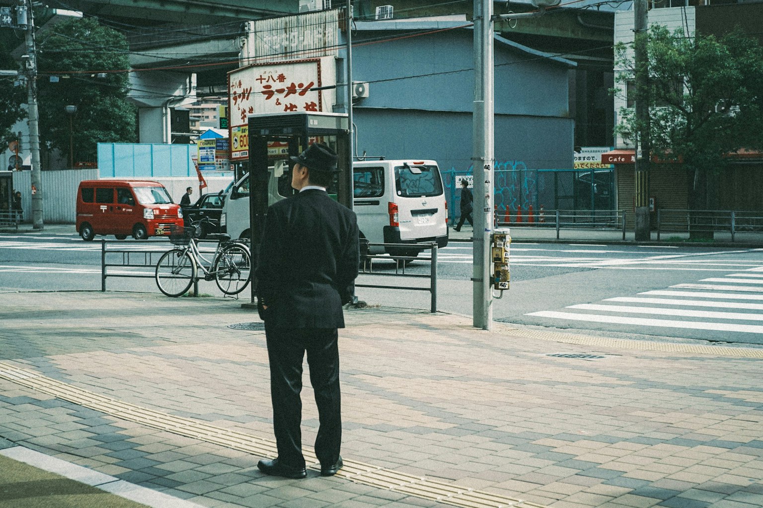 一名穿着黑色西装的男子站在人行横道上，背景为城市风景