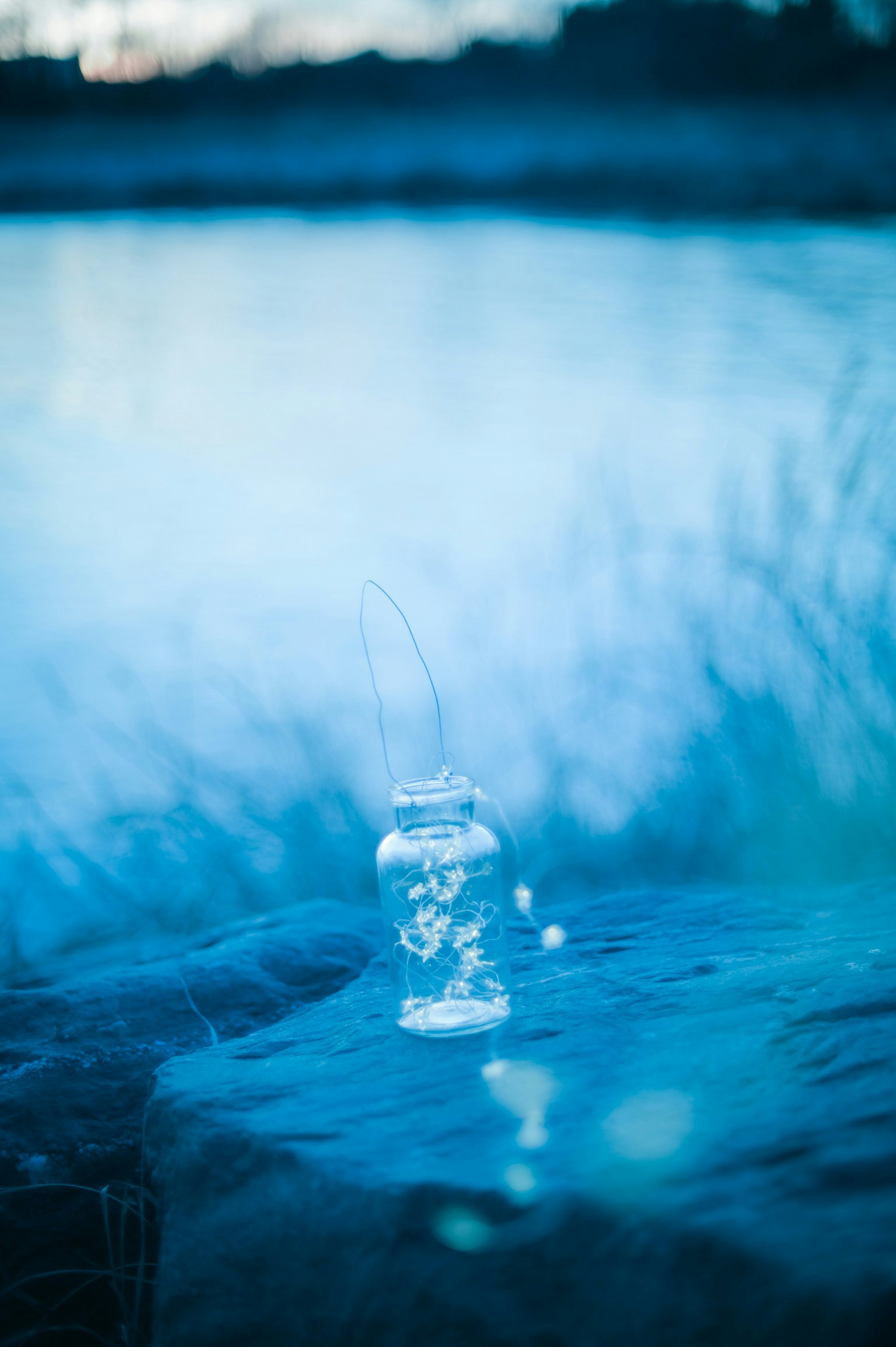 bottiglia di vetro con gocce d’acqua su una superficie d’acqua blu