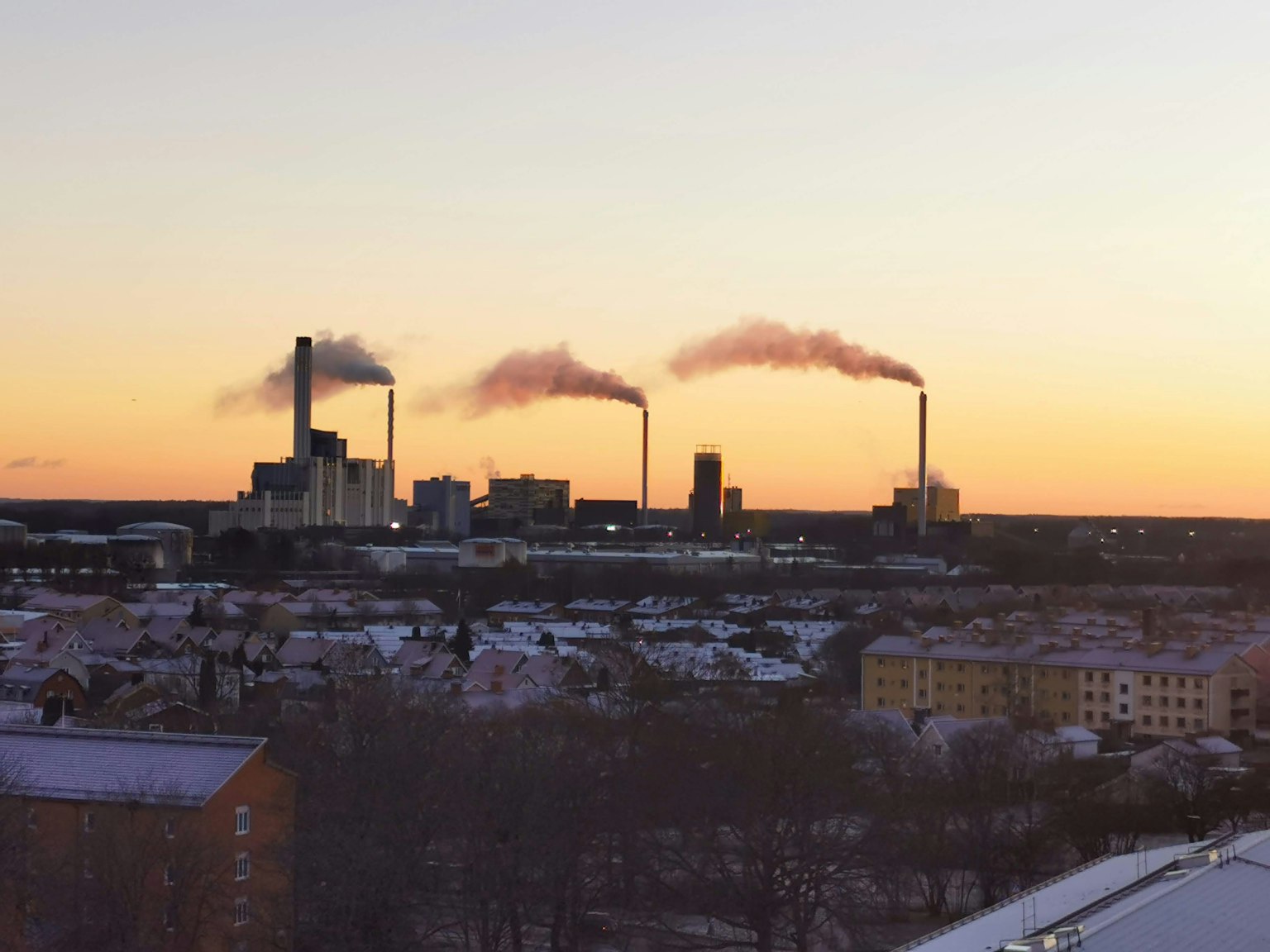 Silueta de fábricas emitiendo humo contra un cielo al atardecer