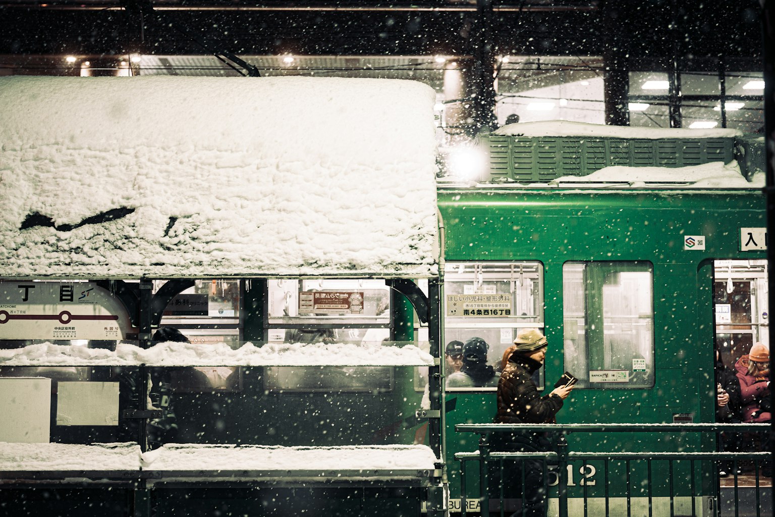 Stazione coperta di neve con un treno verde in attesa