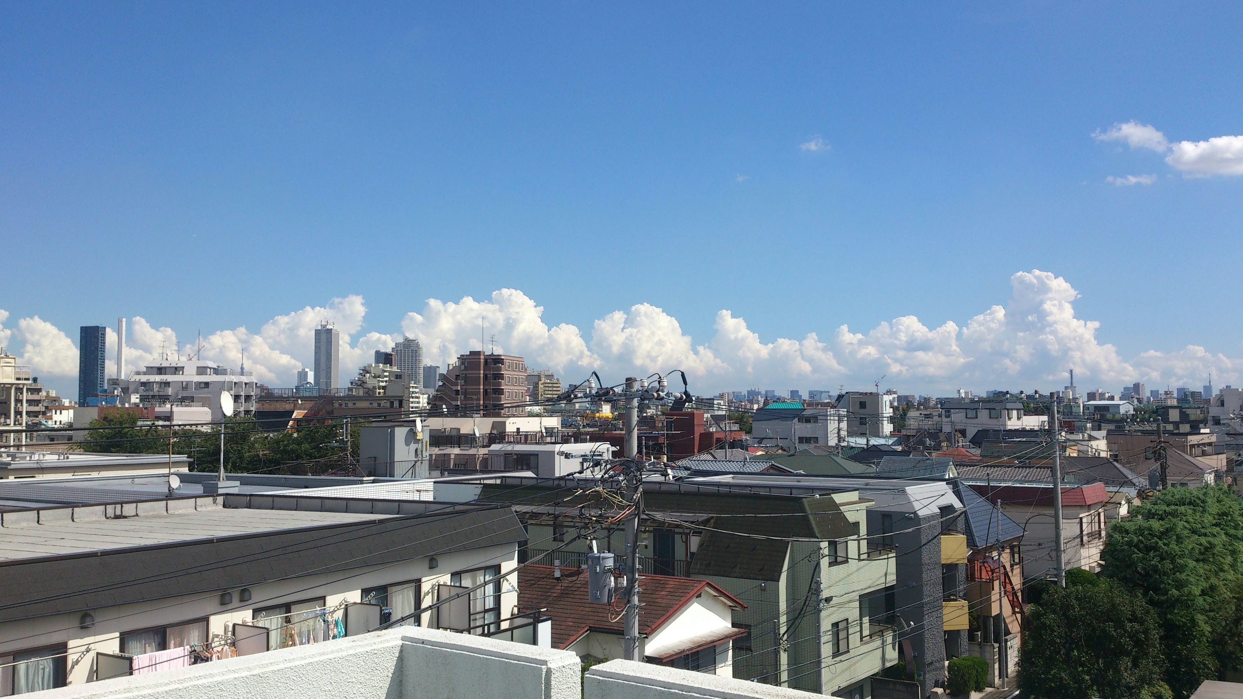 屋上から見下ろす都市の街並みと青空の雲