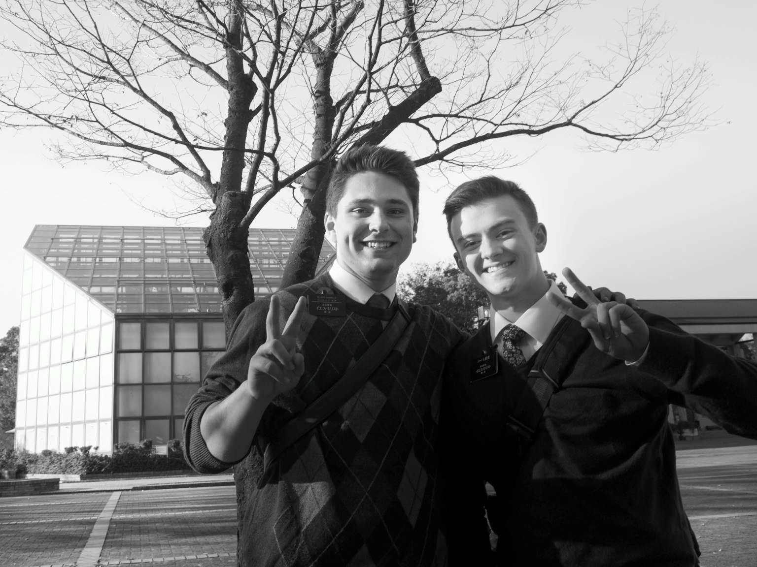 Deux hommes faisant des signes de paix dans une photo en noir et blanc avec un bâtiment et un arbre en arrière-plan