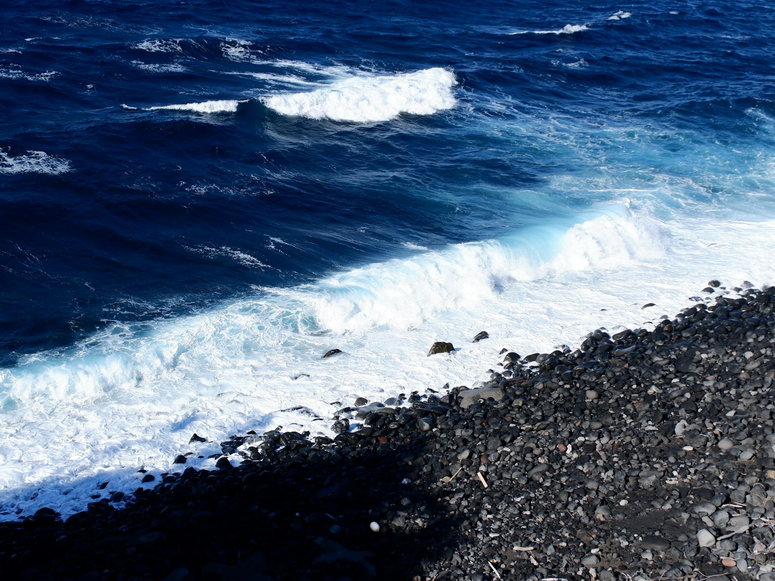 Olas azules del océano rompiendo en una playa rocosa