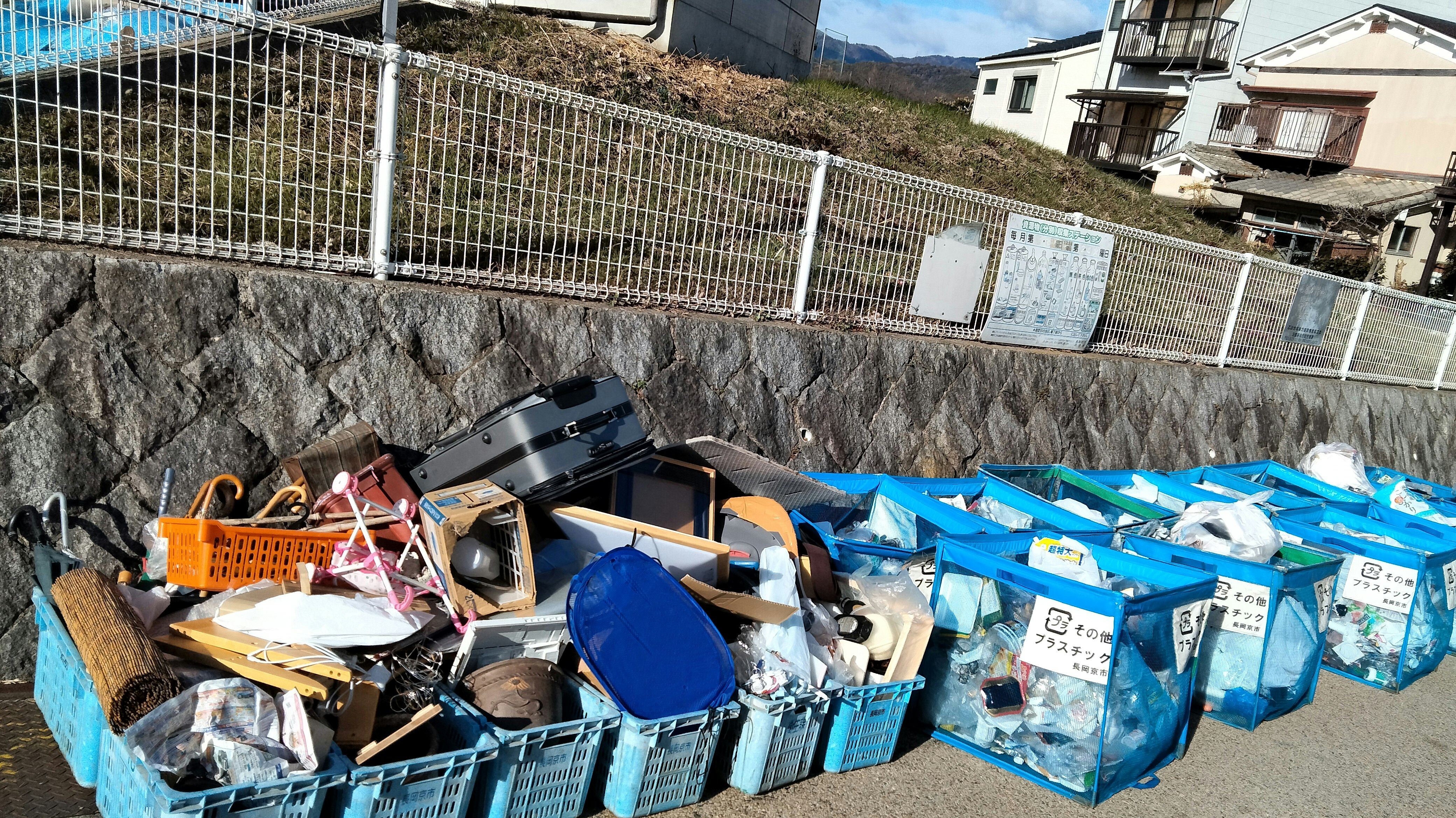 zona de recogida con cajas de cartón y bolsas de basura azules frente a un muro de piedra