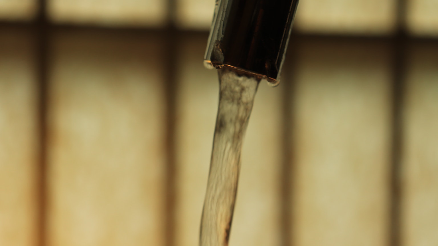 Immagine ravvicinata dell'acqua che scorre da un rubinetto con uno sfondo in legno sfocato