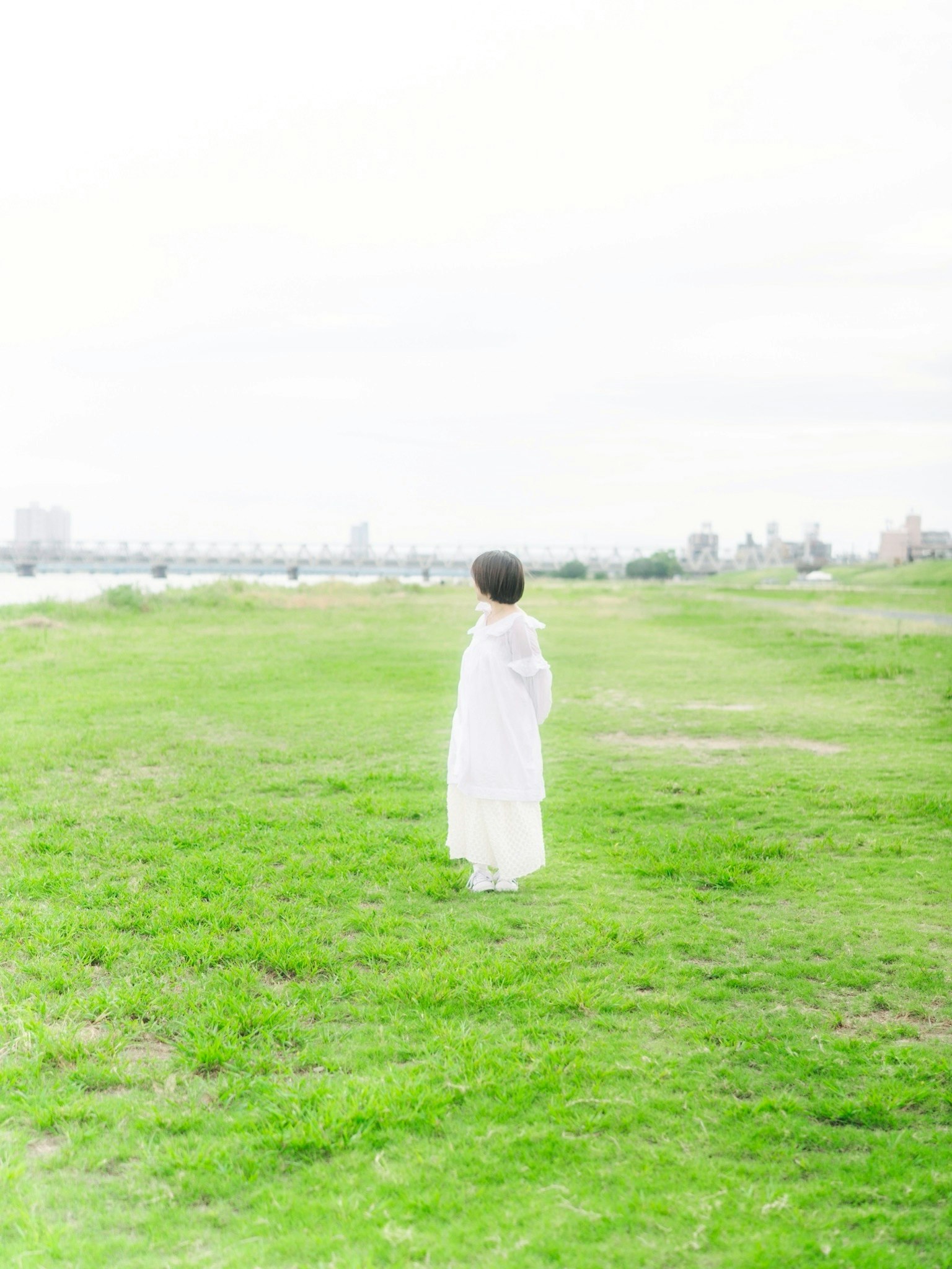 緑の草原に立つ白い服を着た人物の後ろ姿と遠くの都市の景色