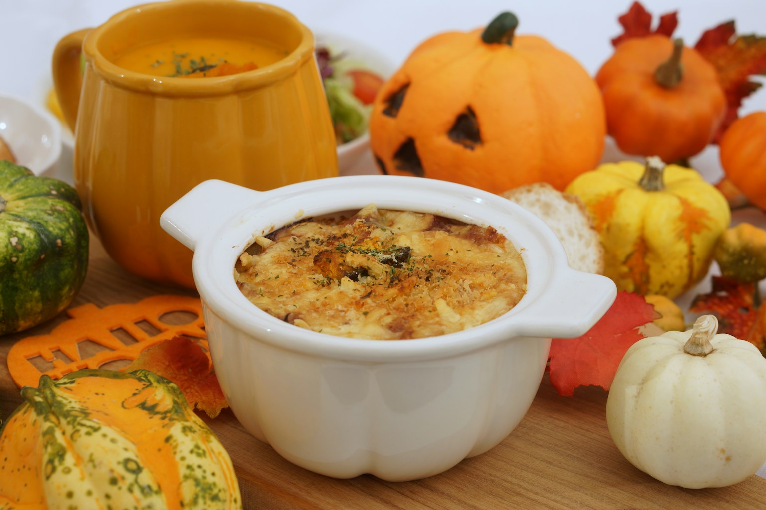 Plato horneado en un tazón blanco rodeado de pequeñas calabazas y decoraciones de otoño