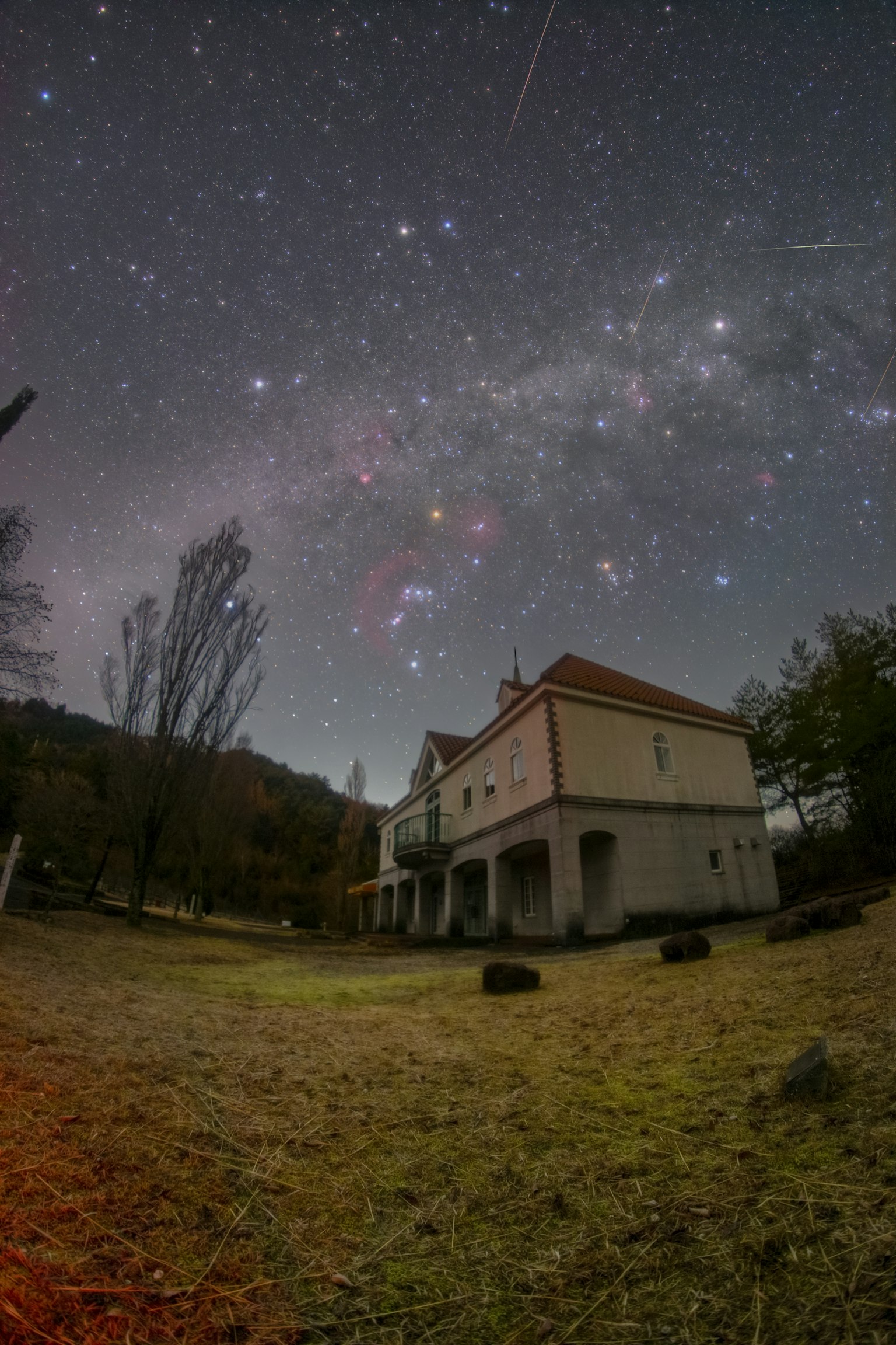 Una casa antigua bajo un cielo estrellado con estrellas fugaces