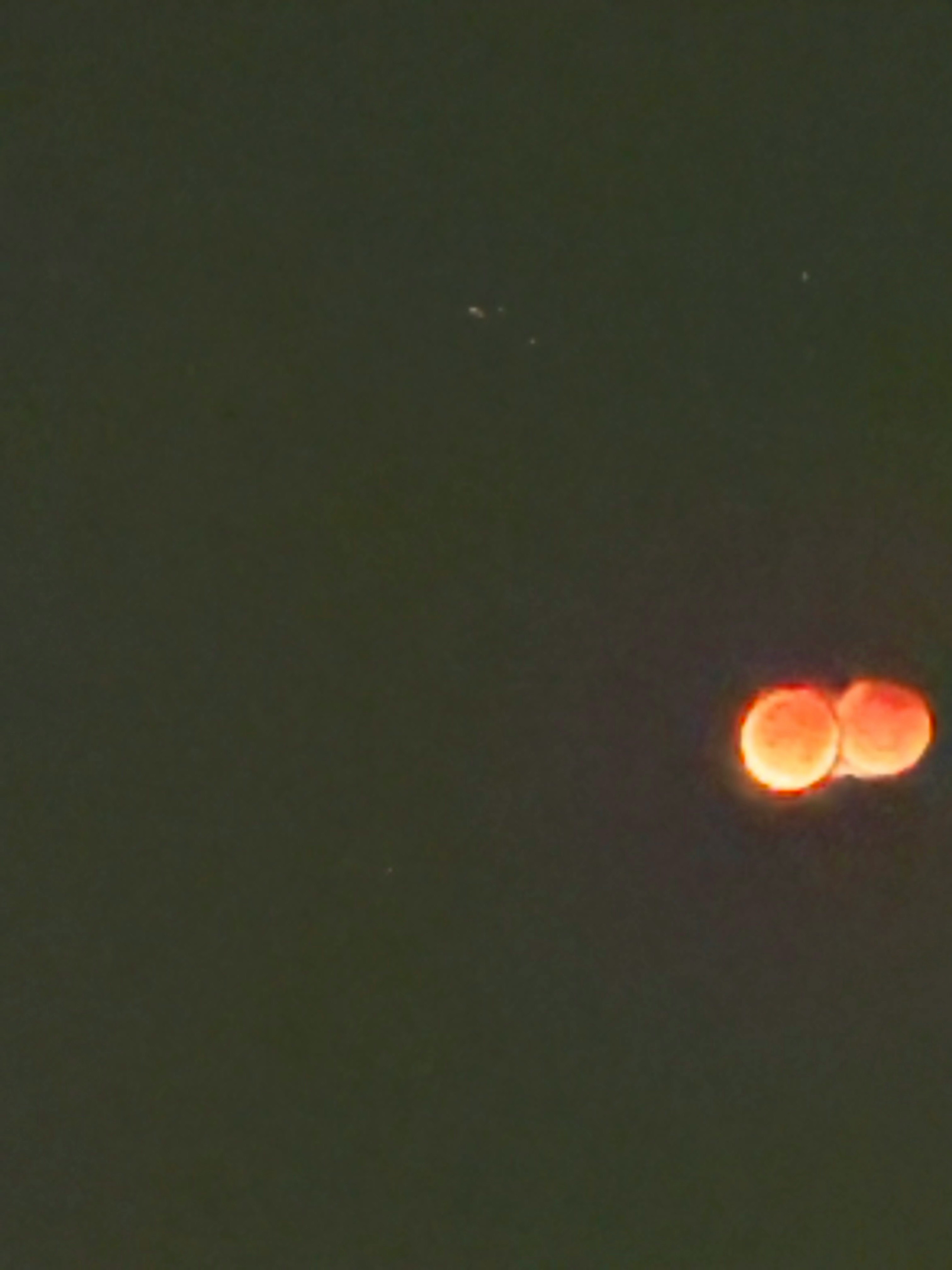 ぼやけた夜空に浮かぶ赤い月のような光