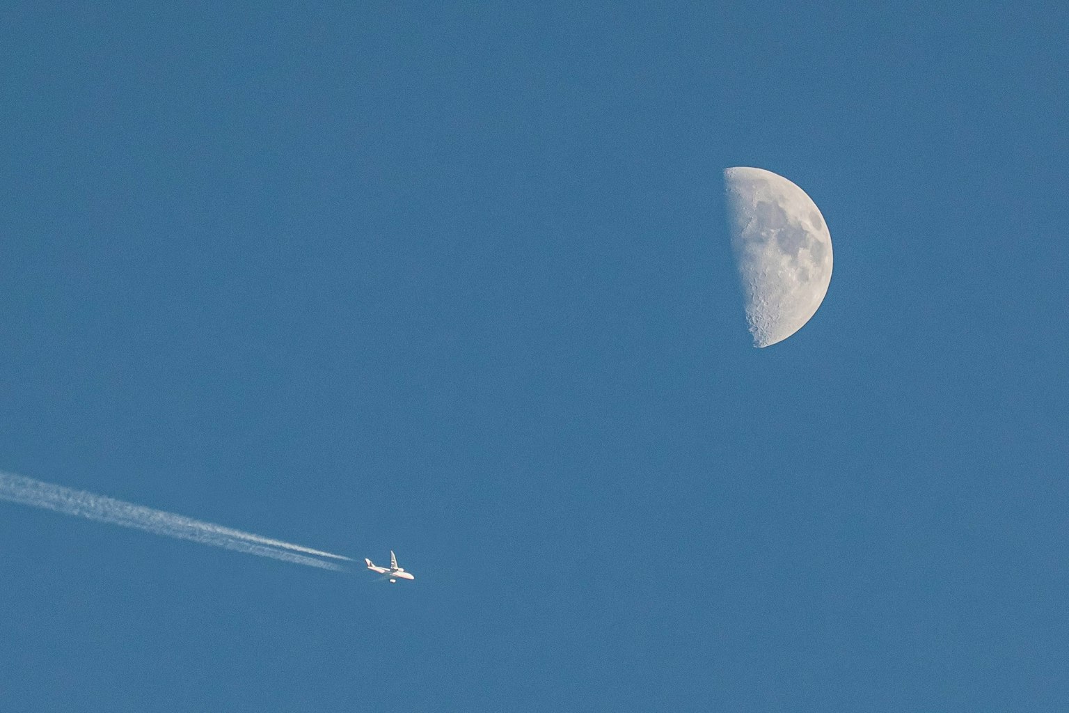 Bulan setengah di langit biru dengan jejak pesawat