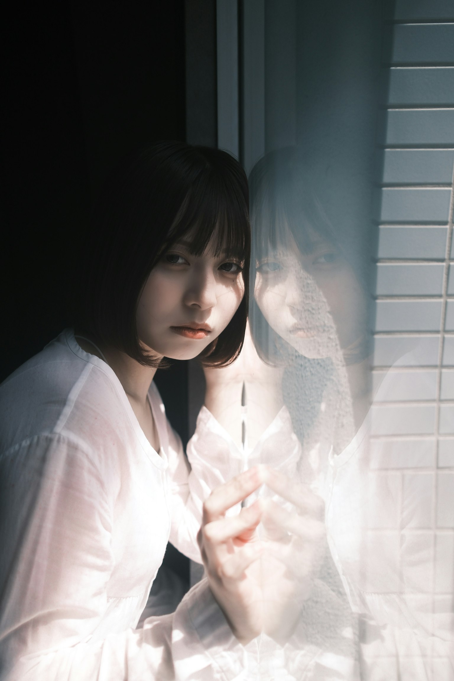 窓辺に座る女性のポートレート 彼女は白いシャツを着ていて 反射が印象的