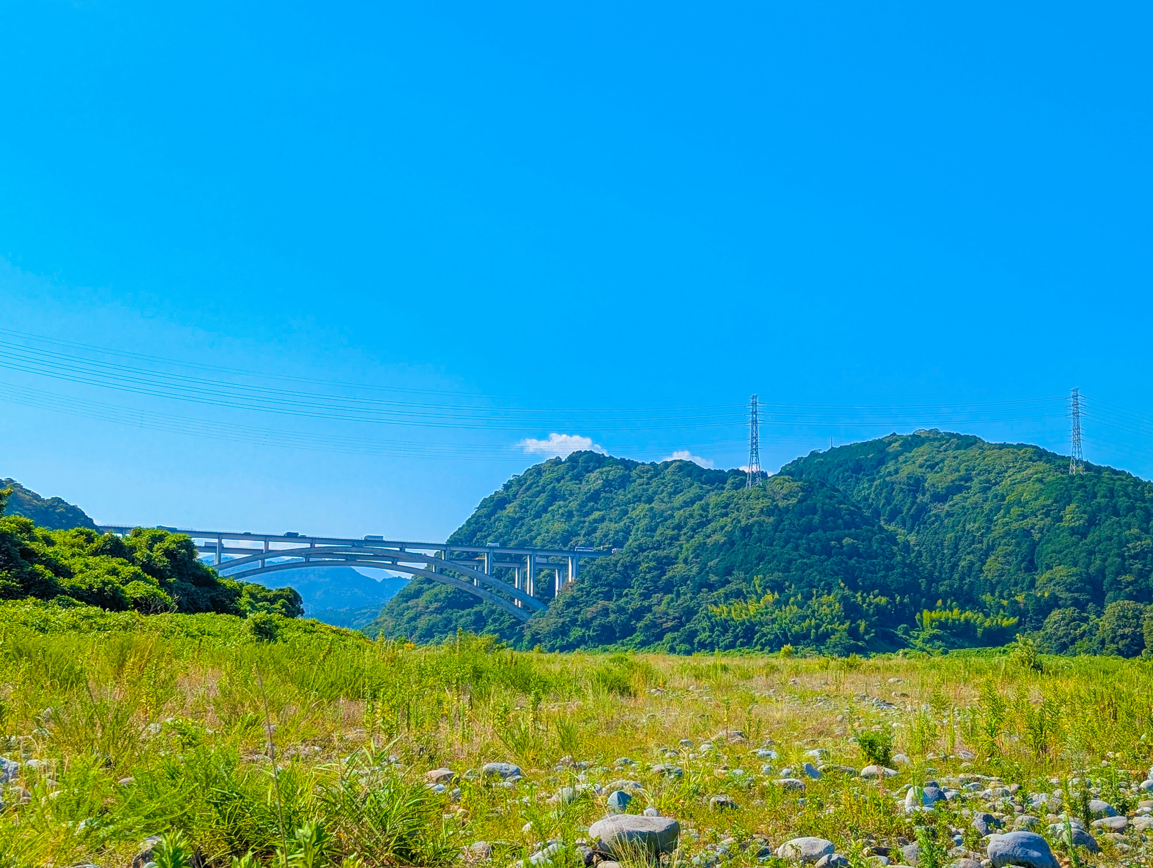 河川敷の草地と緑の山並み、青空の風景画像