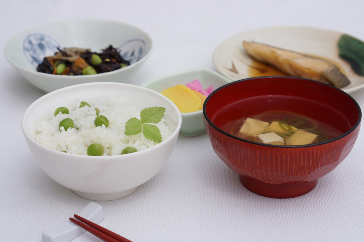 Weißer Reis mit grünen Erbsen in einer Schüssel rote Miso-Suppe in einer Schüssel verschiedene kleine Gerichte der japanischen Küche