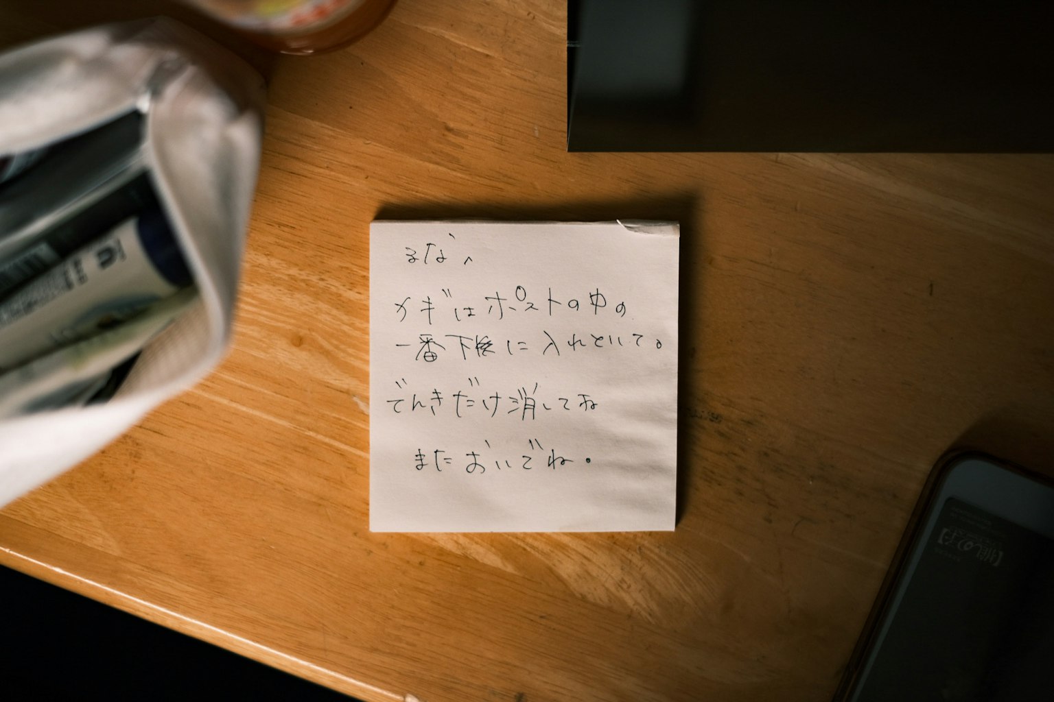 Pesan tulisan tangan dalam bahasa Jepang di atas kertas catatan yang diletakkan di atas meja kayu