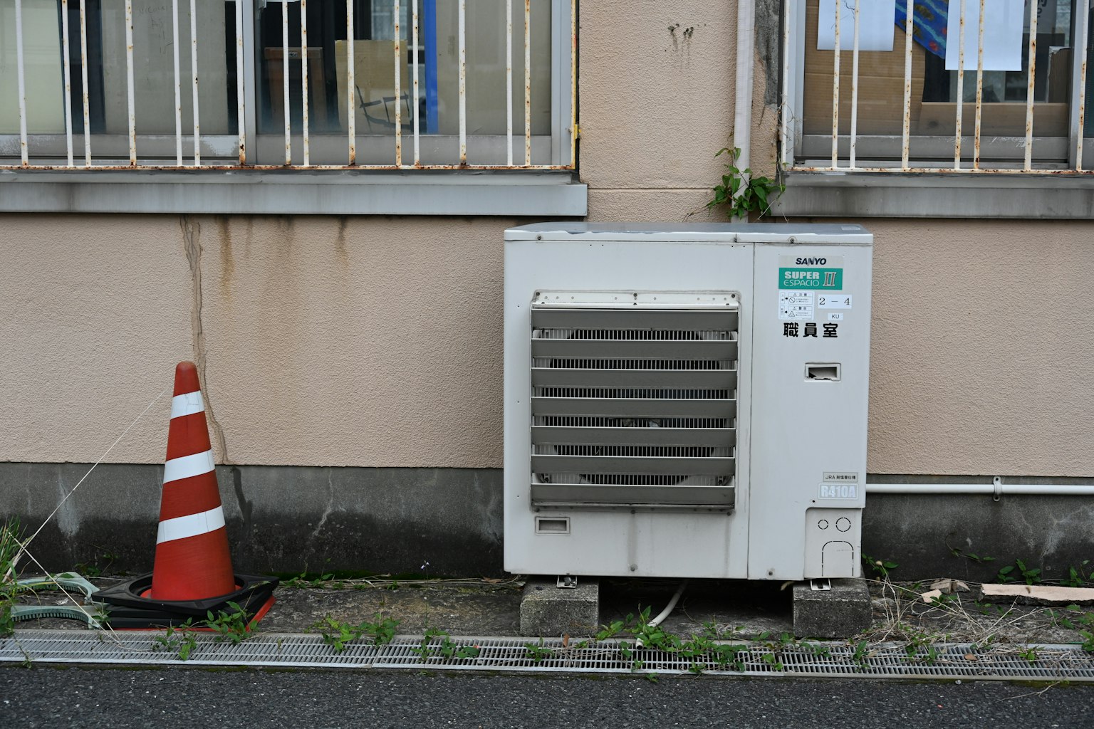 Unità esterna di climatizzazione accanto a un muro con un cono stradale rosso
