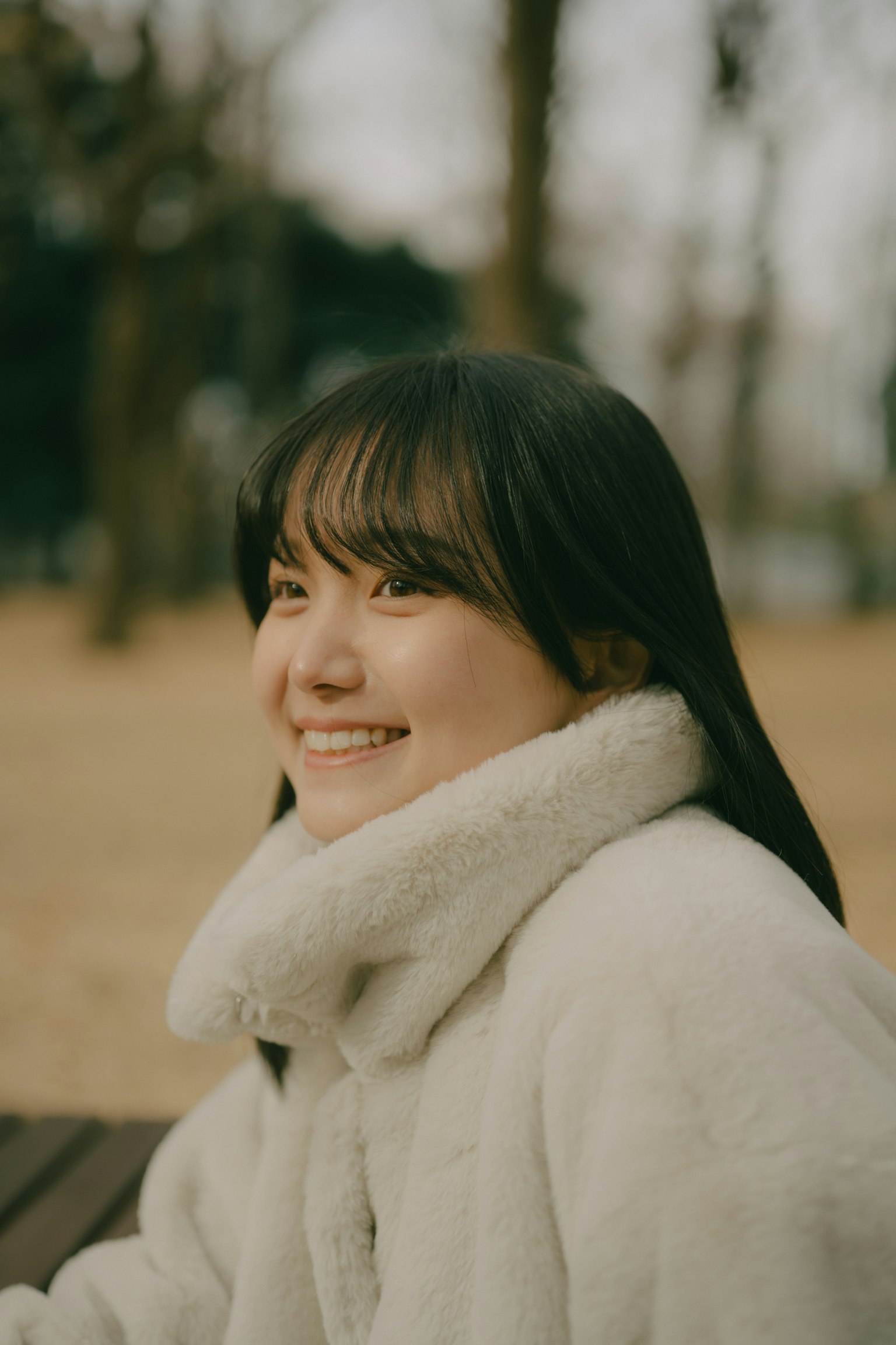 Una donna sorridente che indossa un cappotto bianco in un parco
