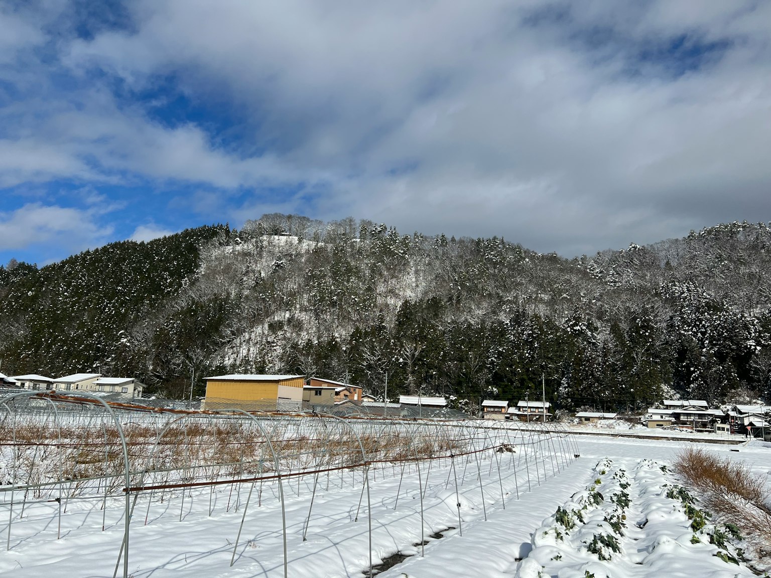 Snow-covered landscape with mountains and farm under blue sky