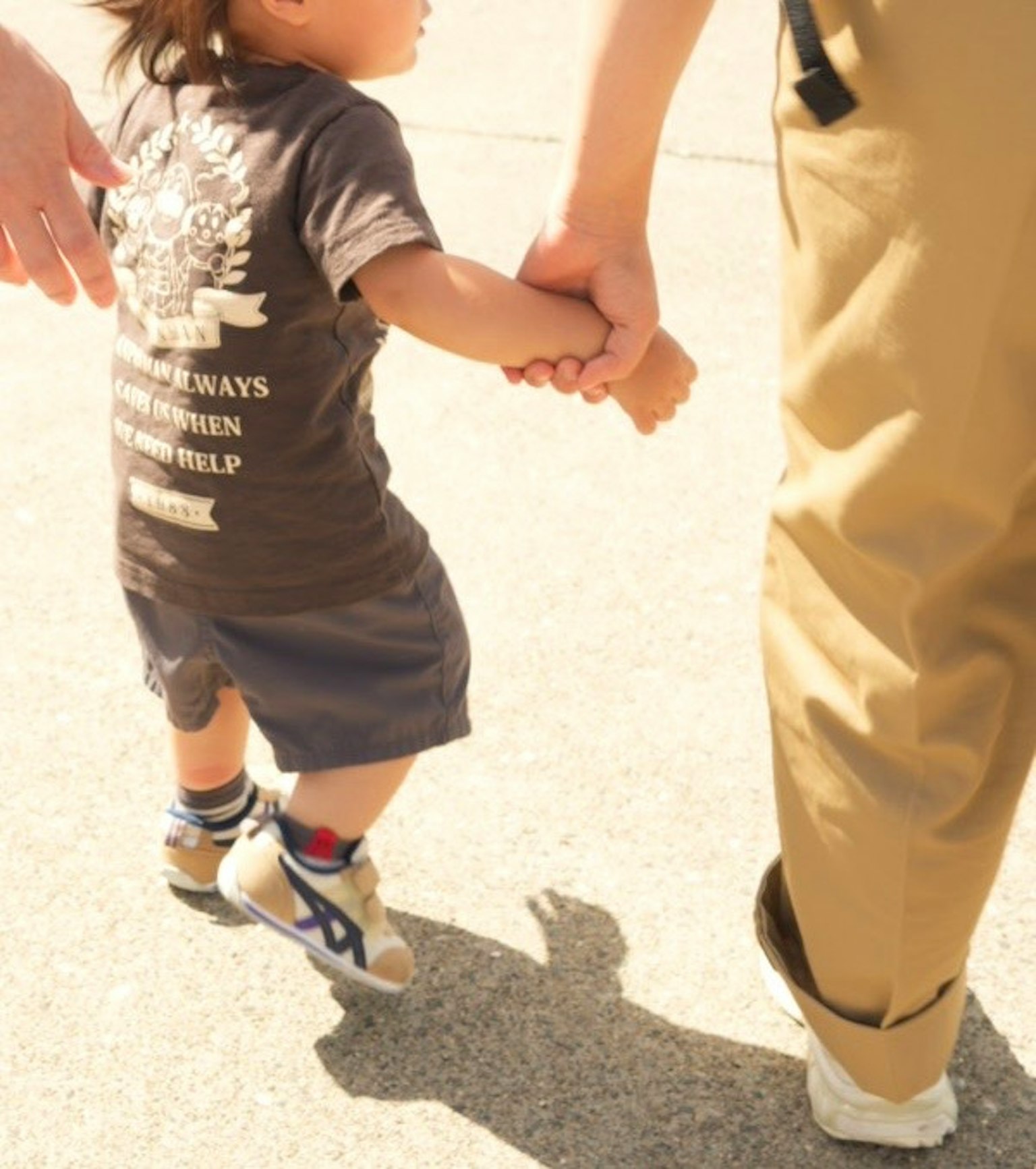 子供が大人の手をつないで歩いている様子 明るい日差しの中での親子の絆