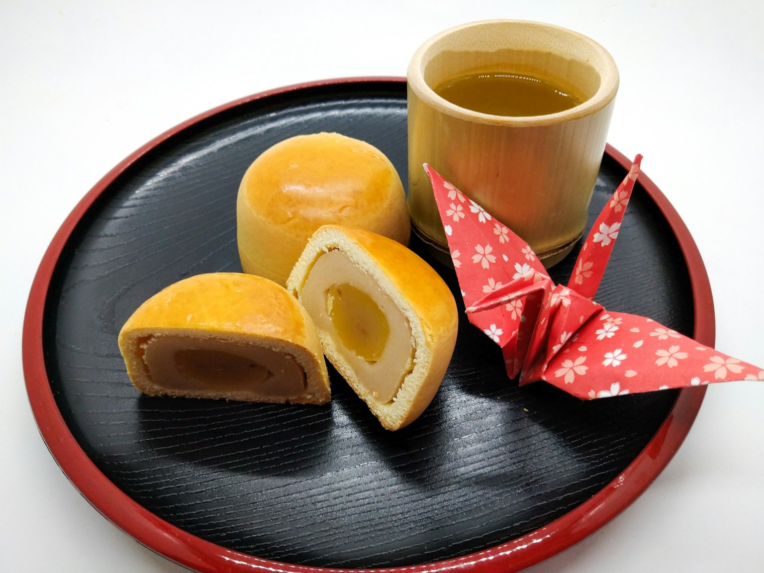 Una selezione di dolci giapponesi su un piatto nero con una tazza di tè e una gru di origami