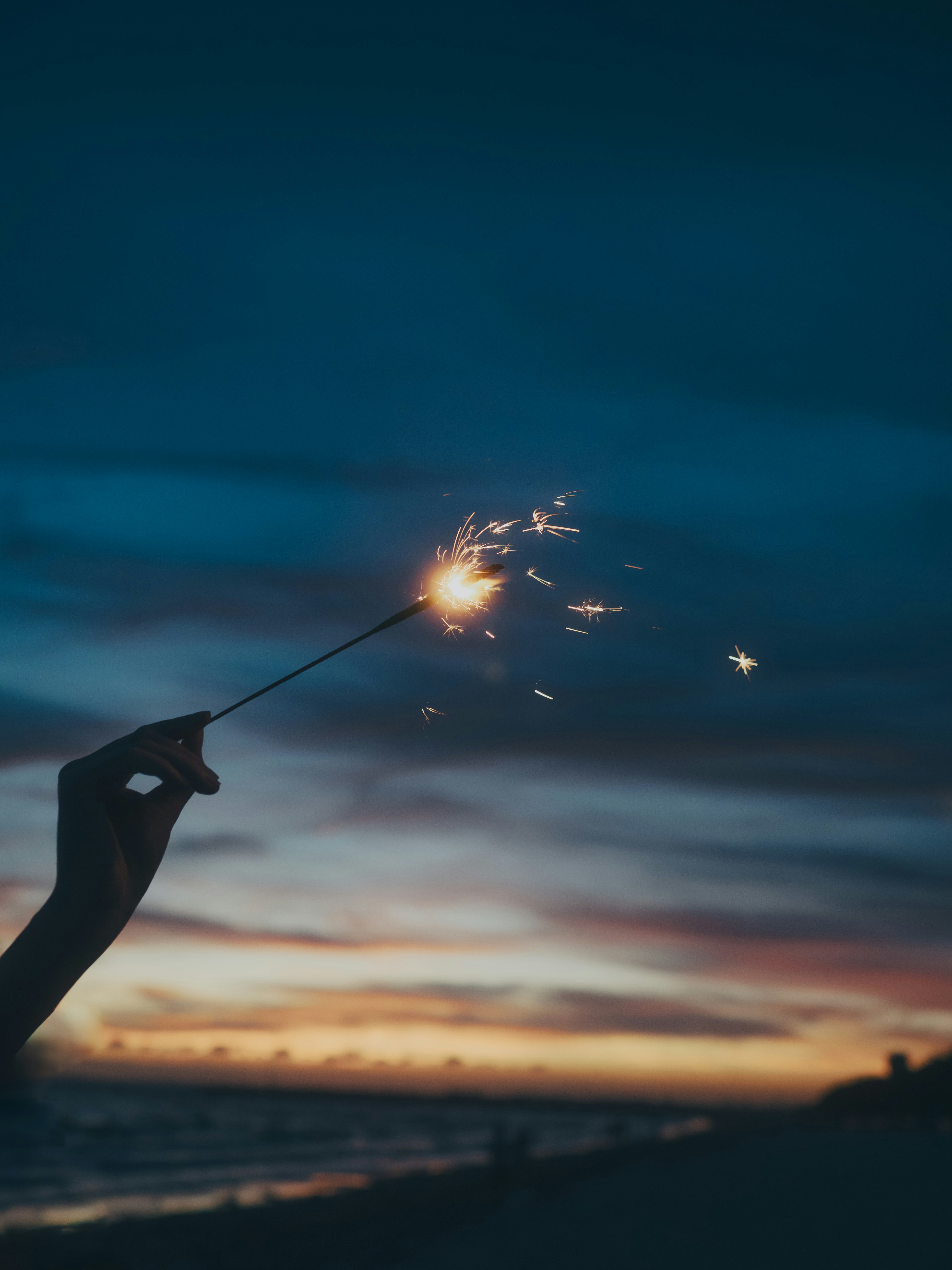 夕暮れの空で手持ち花火を打ち上げる人のシルエット