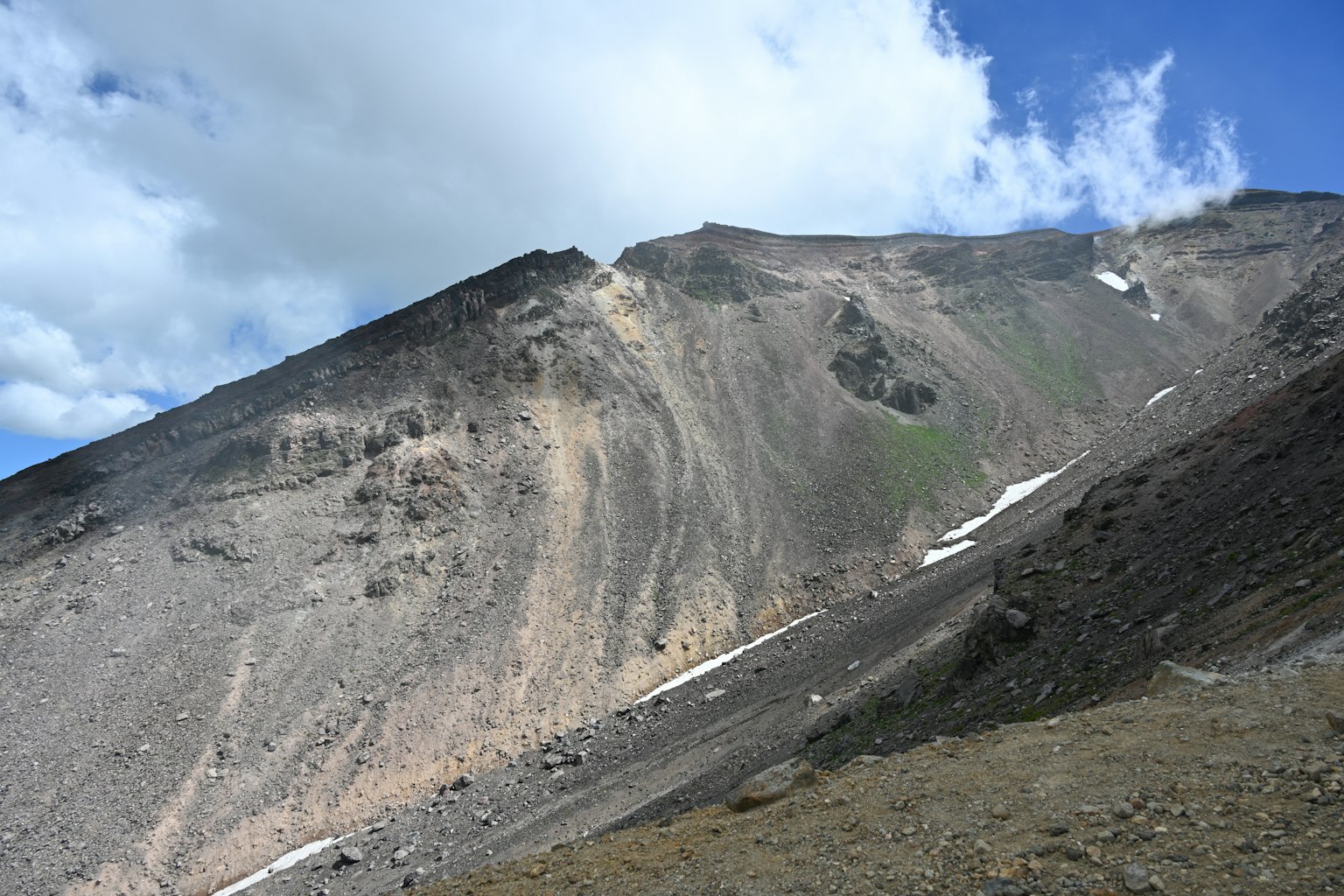Pente de montagne escarpée sous un ciel bleu avec des nuages