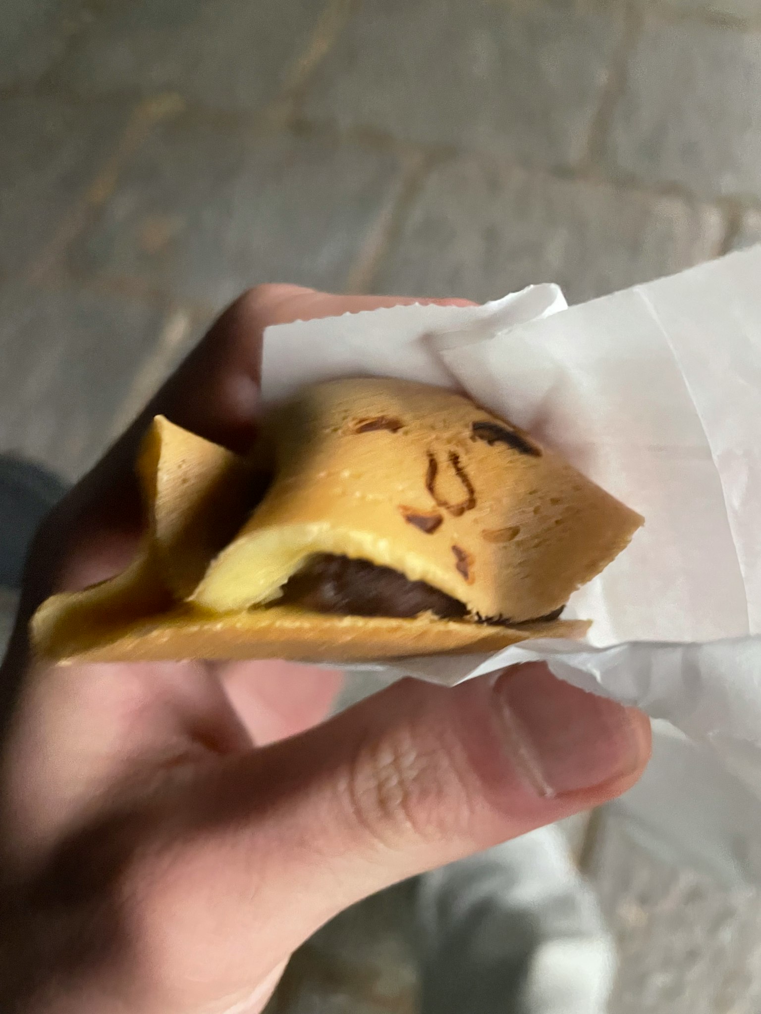 Sebuah tangan memegang crepe lipat dengan isian cokelat dan desain wajah lucu
