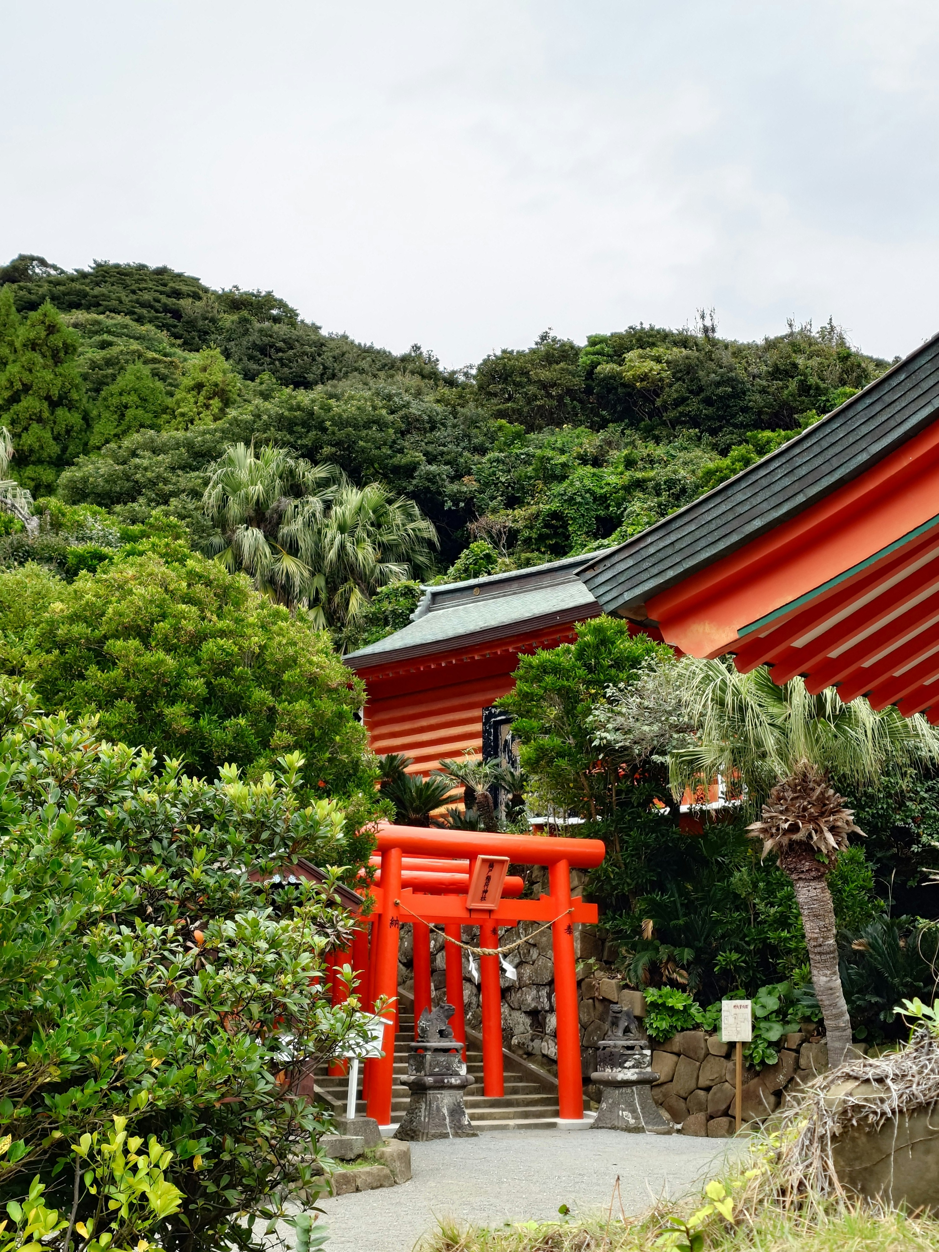 緑の丘に囲まれた朱色の鳥居と社殿のある神聖な場所