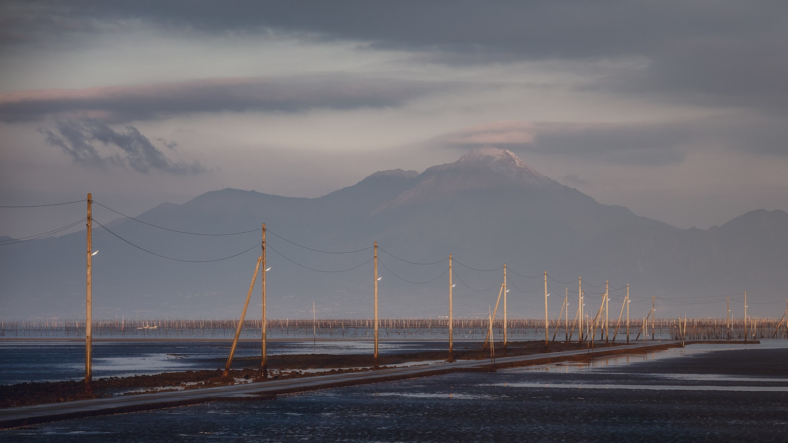 Landscape featuring power poles lined up under a calm sky with distant mountains