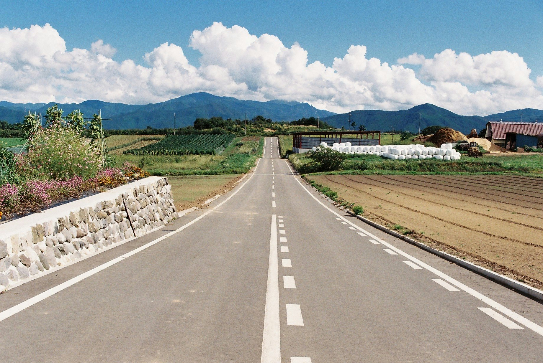 畑と山並みを望む直線の田舎道