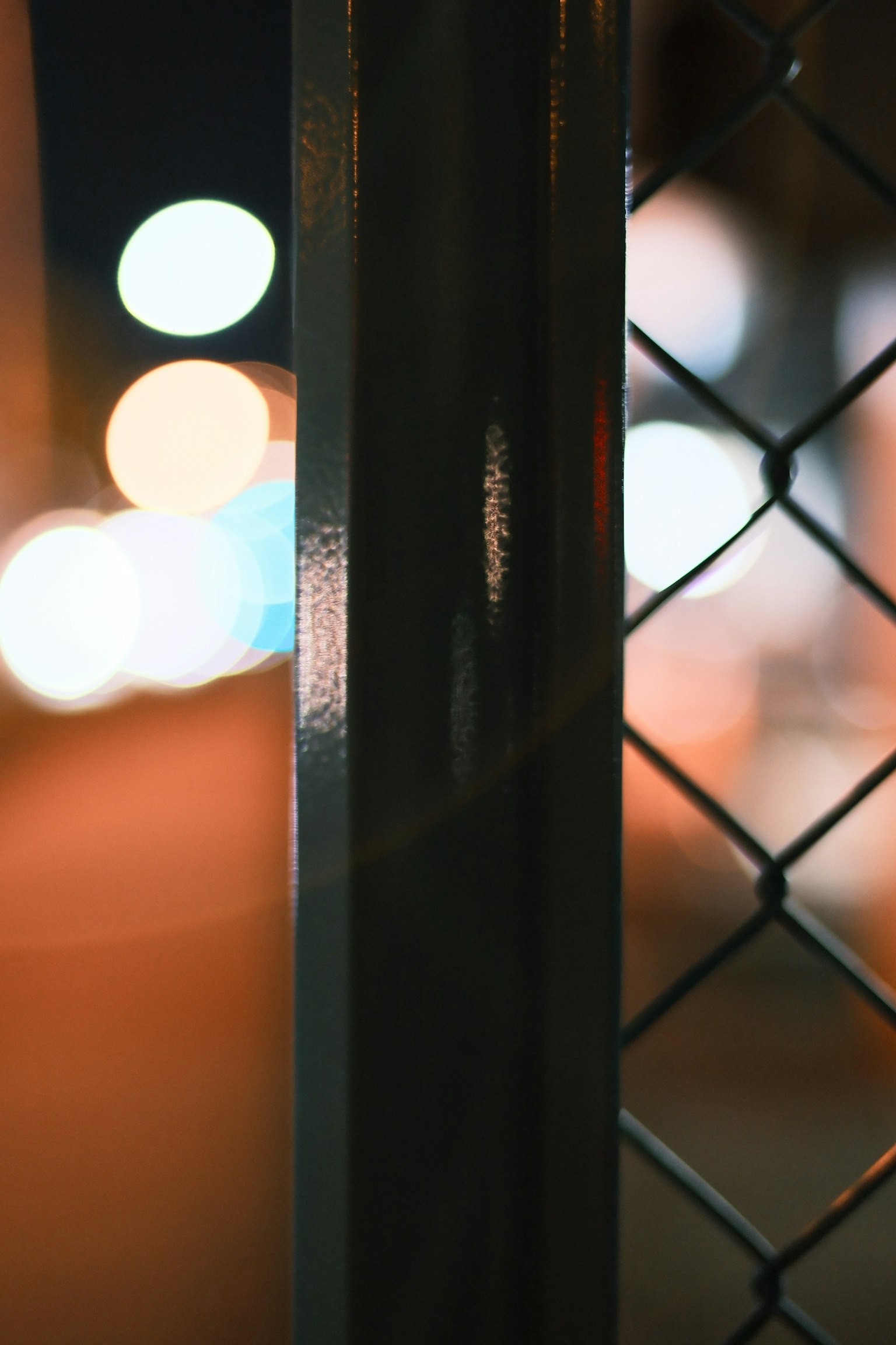 Primer plano de un poste de cercado de metal con luces de ciudad borrosas de noche